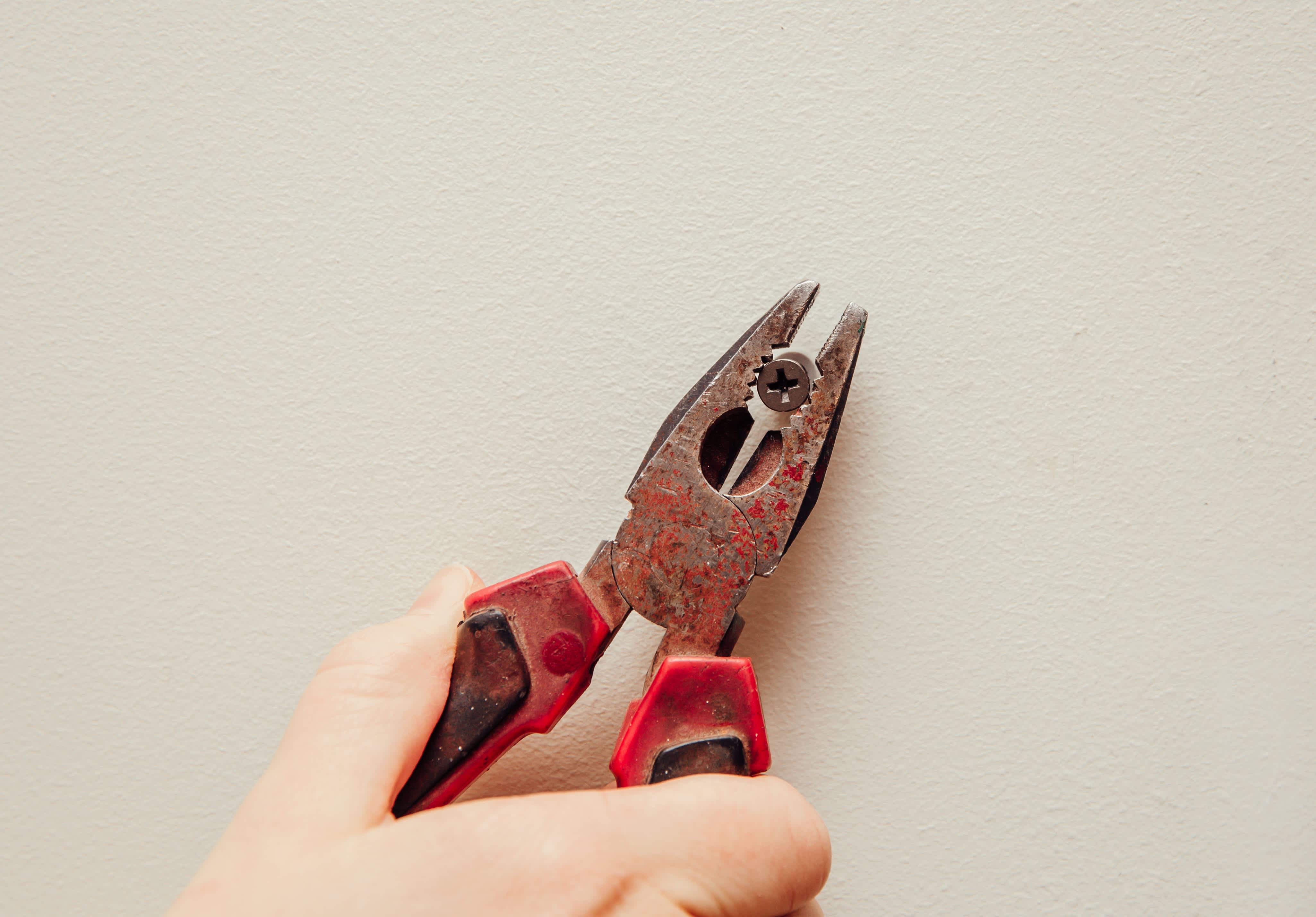 A person removing an old screw and dowel from the wall with a pair of pliers