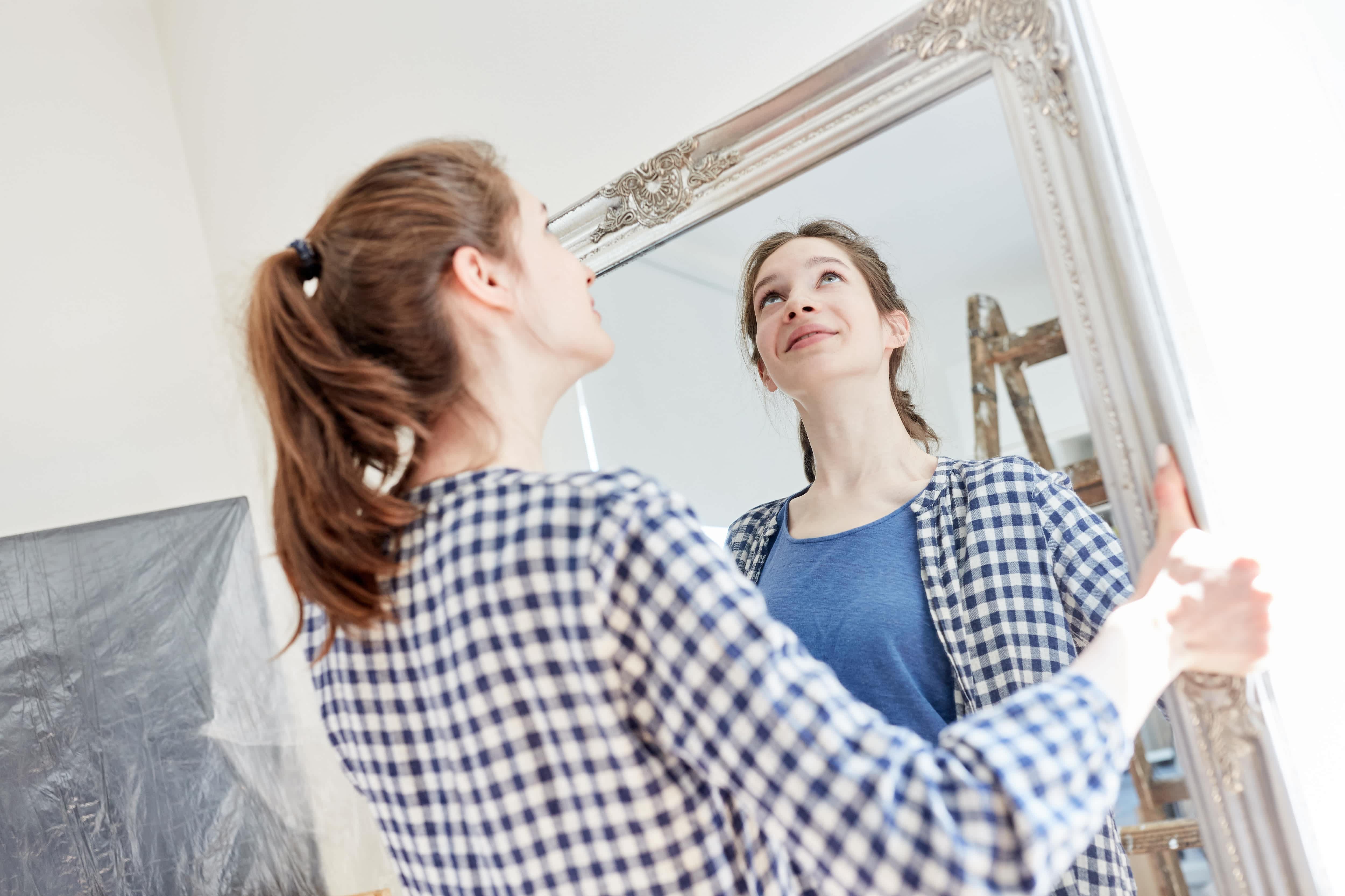 A woman getting ready to hang a heavy framed mirror on a wall