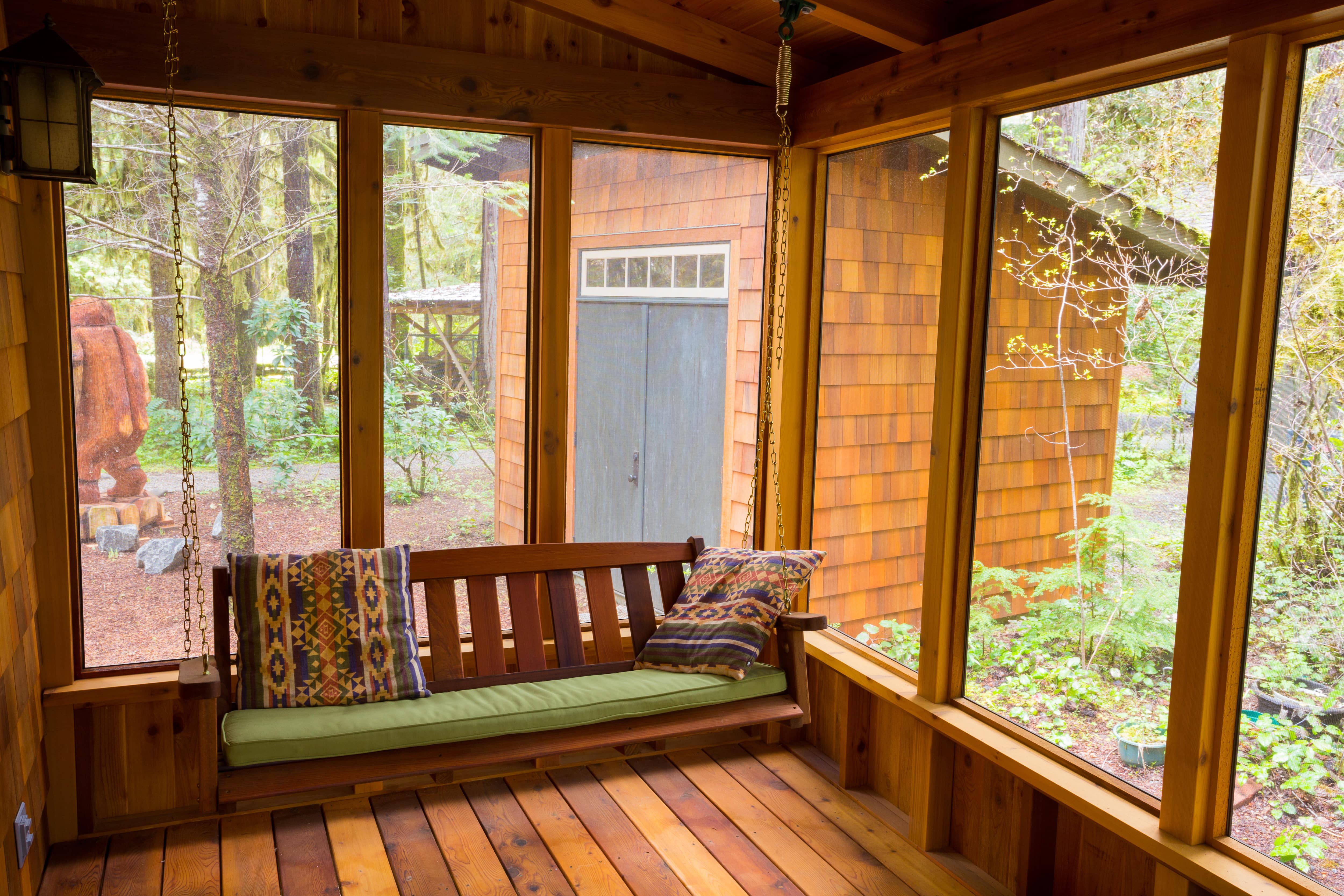 A wooden bench swing with cushions hanging from the ceiling of a screened porch
