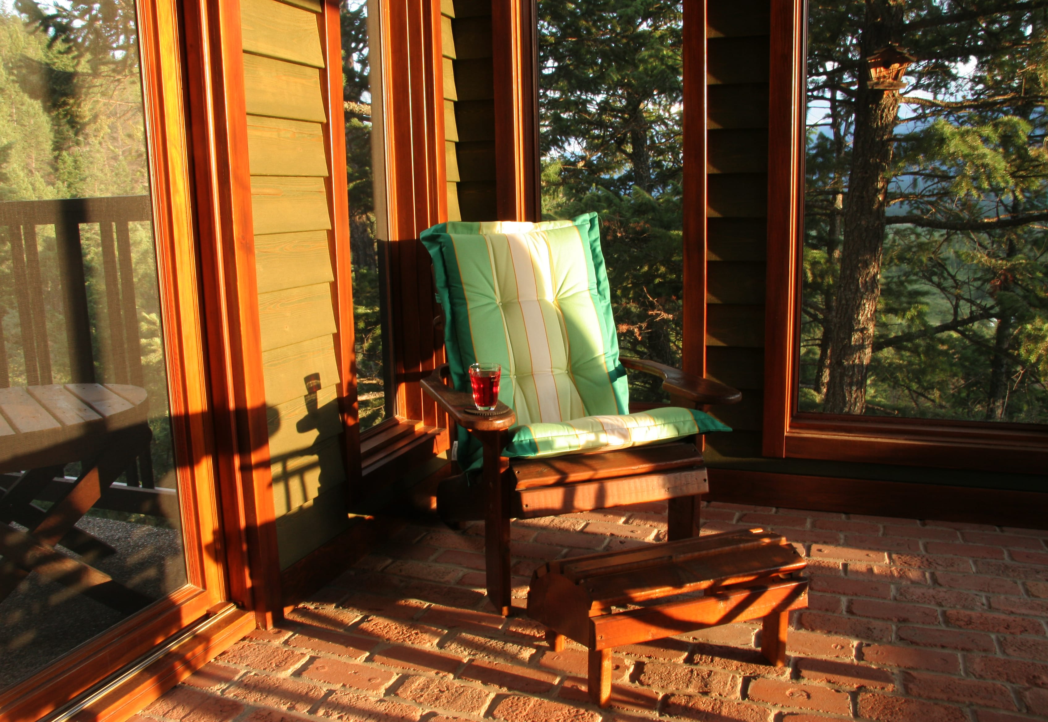 A cushioned wooden chair on a screened-in porch at sunset