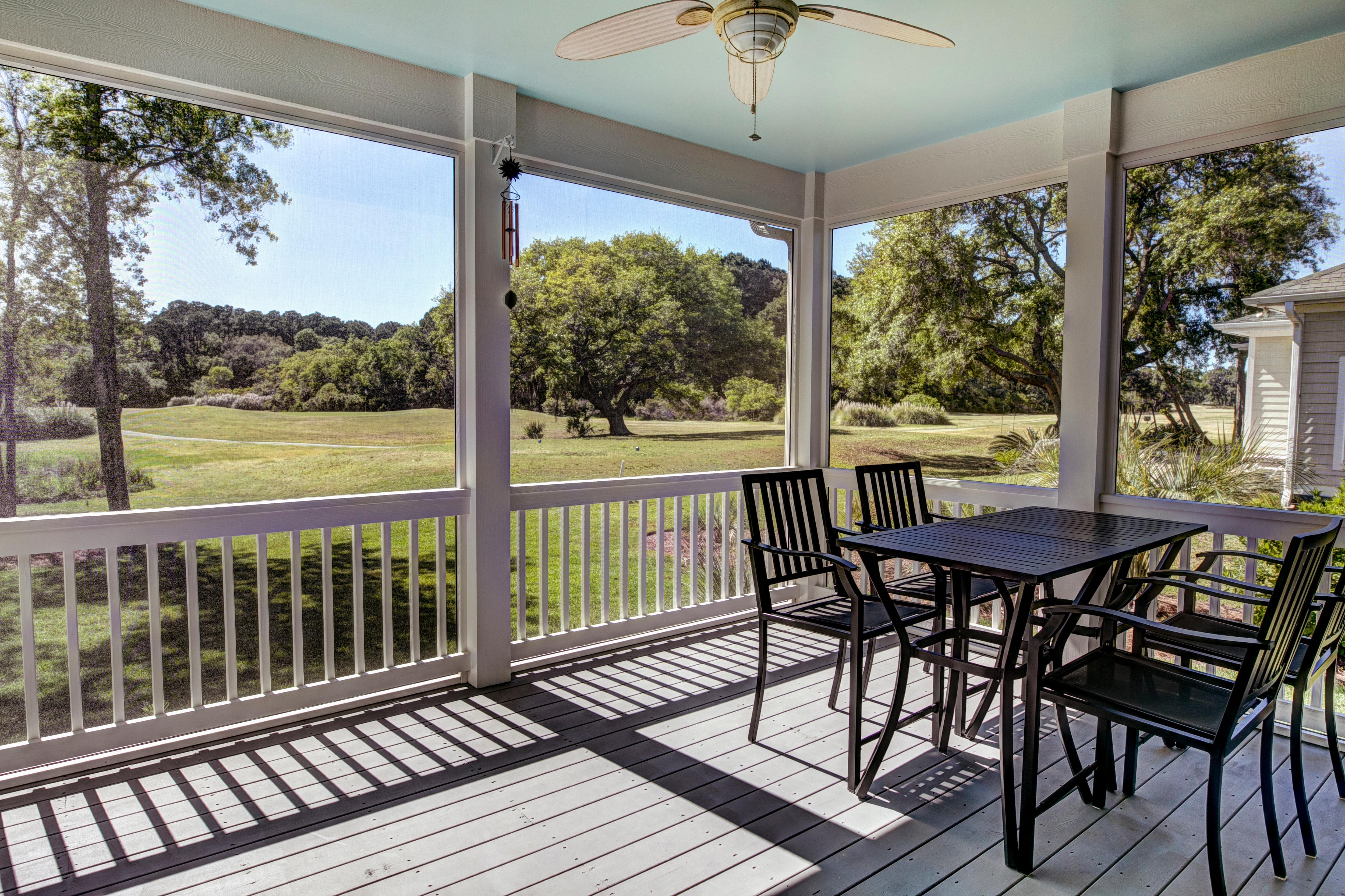 A screened-in porch with a black table and chair set overlooking open land