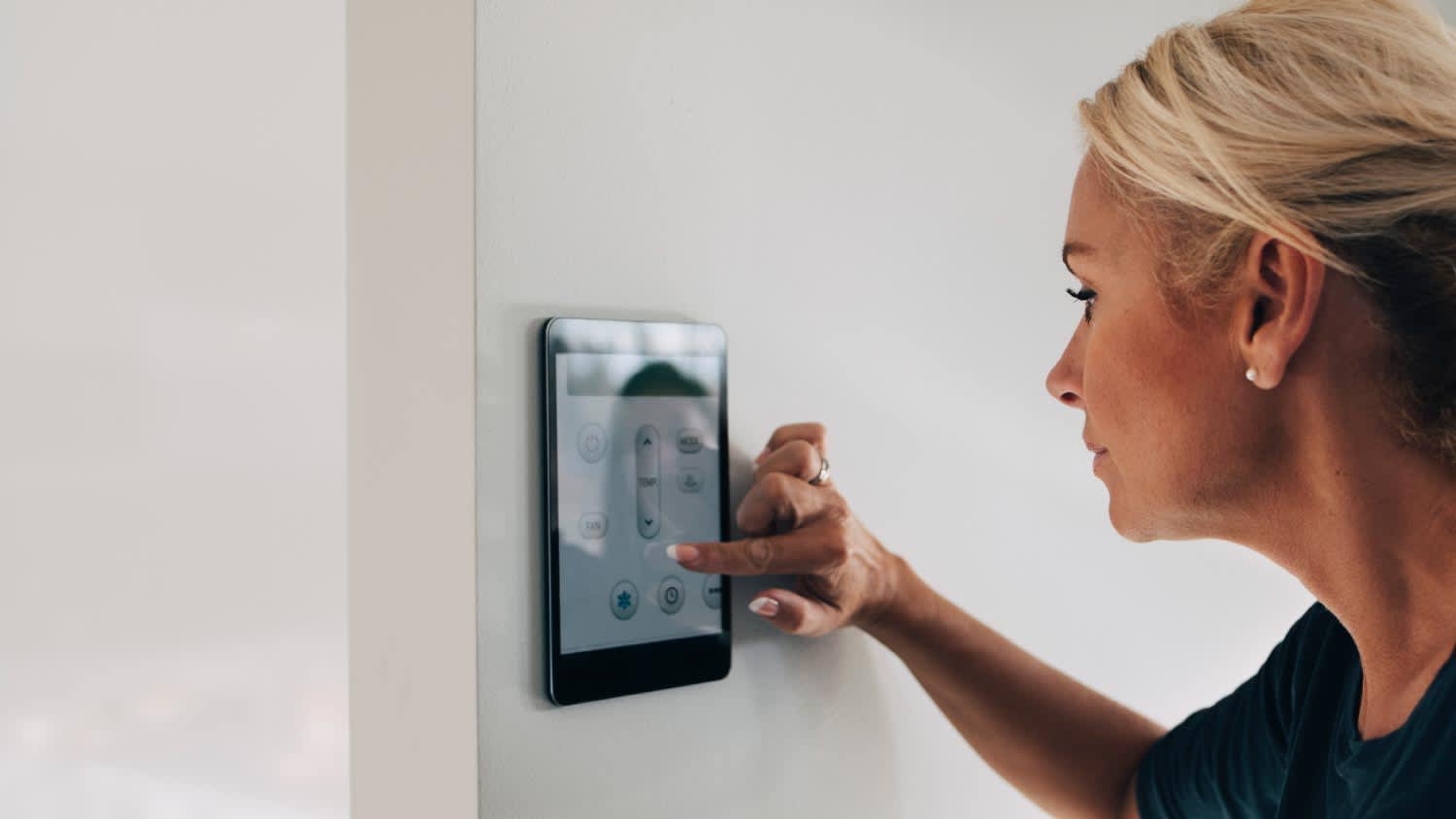 A blond woman adjusting thermostat using digital tablet