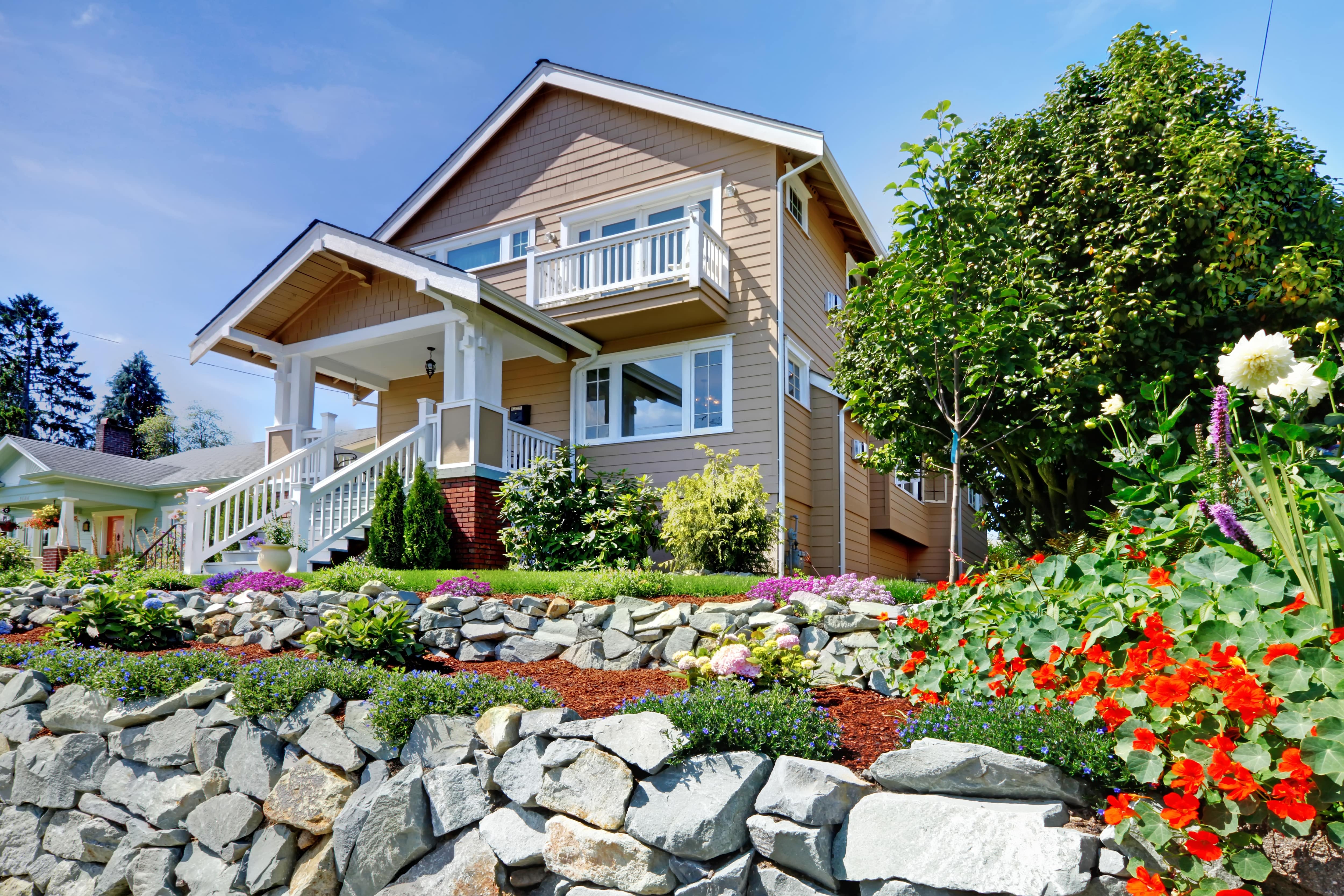 Tan house with white trim with rock hardscape and flowers in the front yard