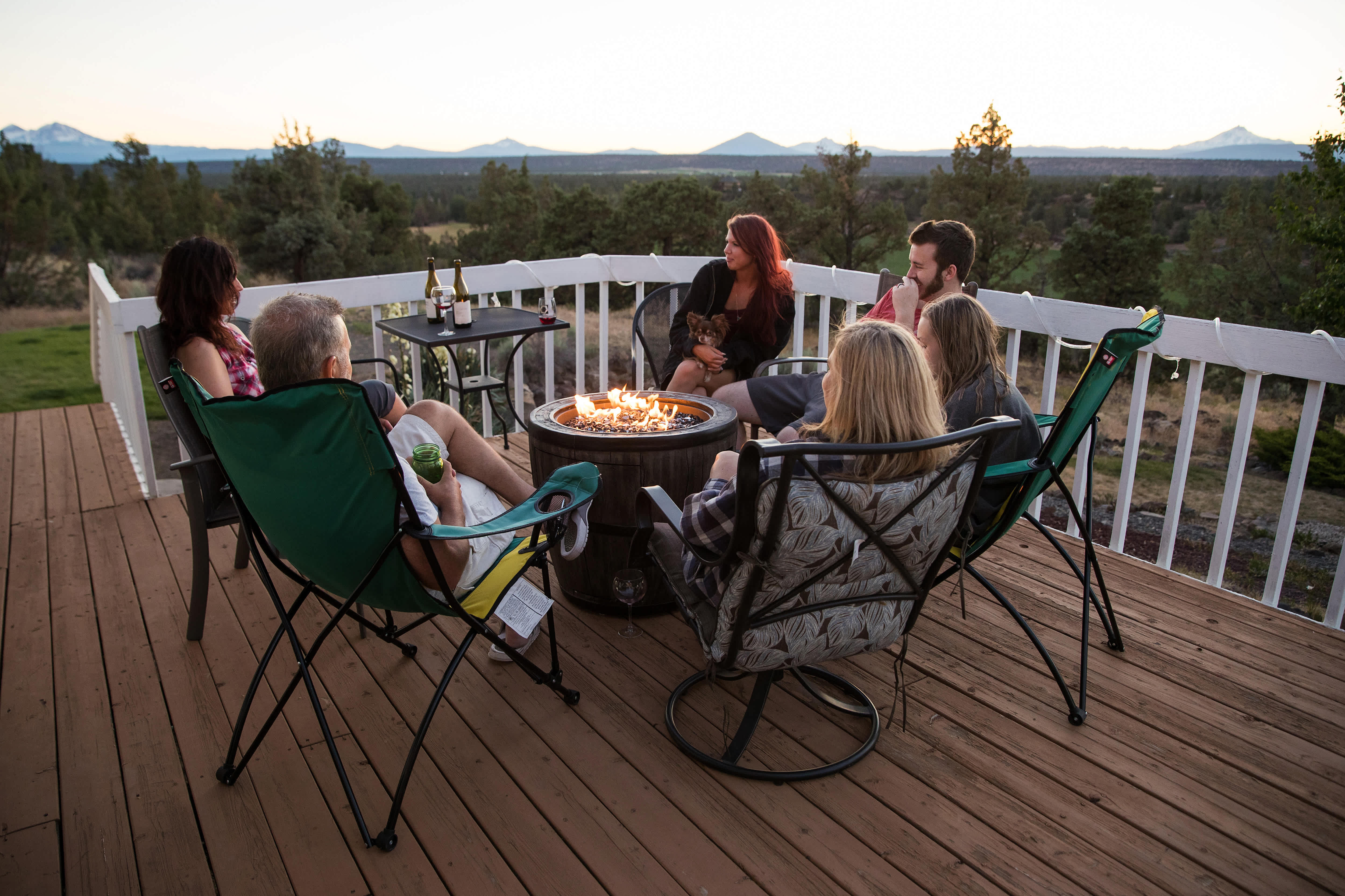 People sitting around a fire pit on a deck outside at dusk