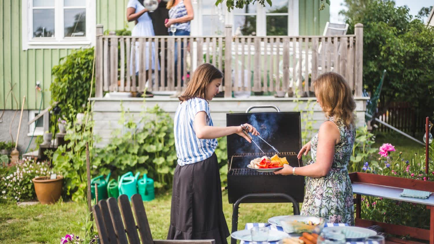 Mother and daughter preparing food on barbecue in backyard party