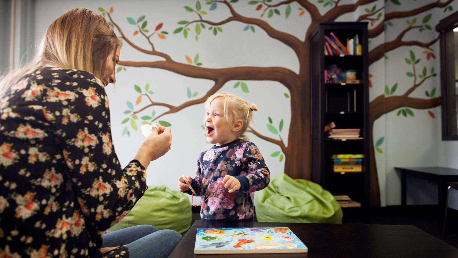 A mother playing with her daughter in playroom with mural on wall
