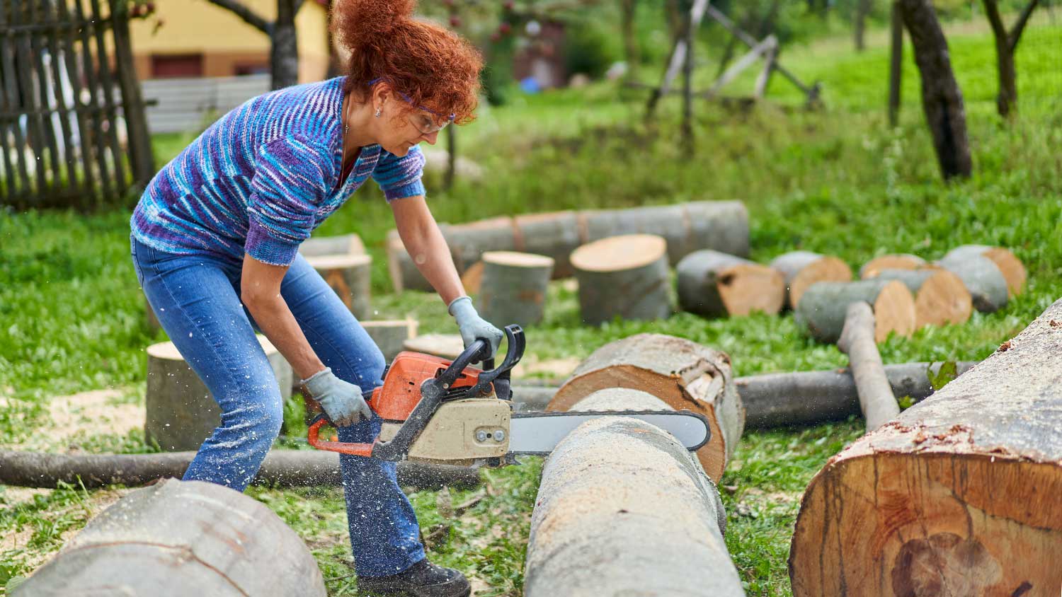 Woman using chainsaw to cut tree logs in her yard