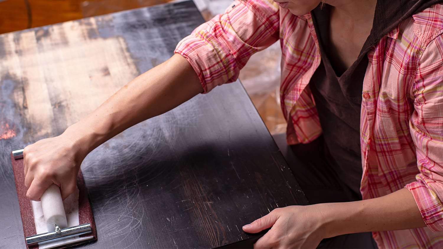 Woman resurfacing a black wooden table