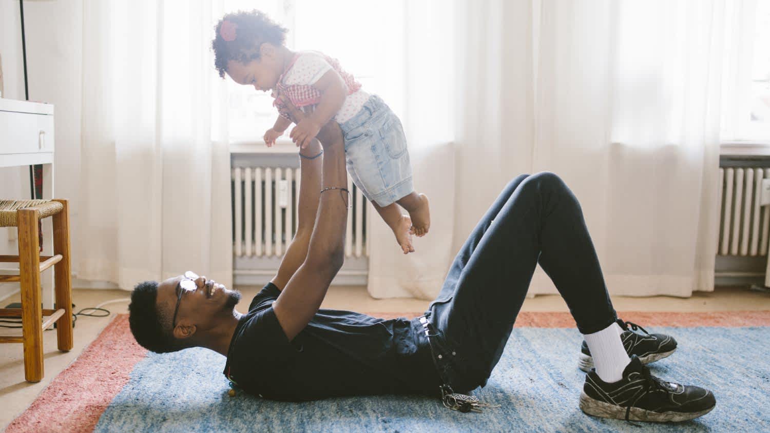 Father lifting daughter while lying on carpet at home