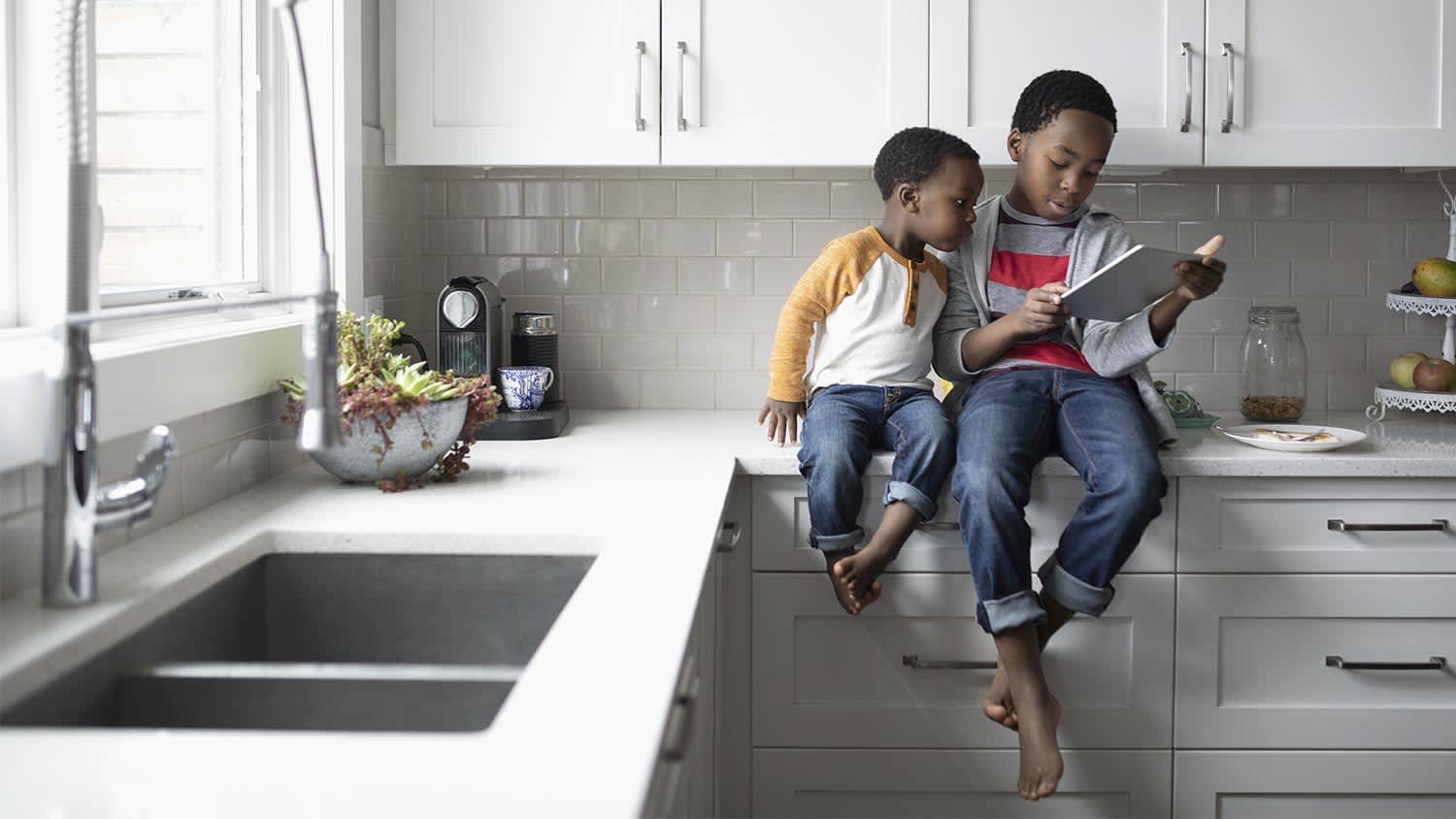 Two kids sit on kitchen counter while looking at ipad