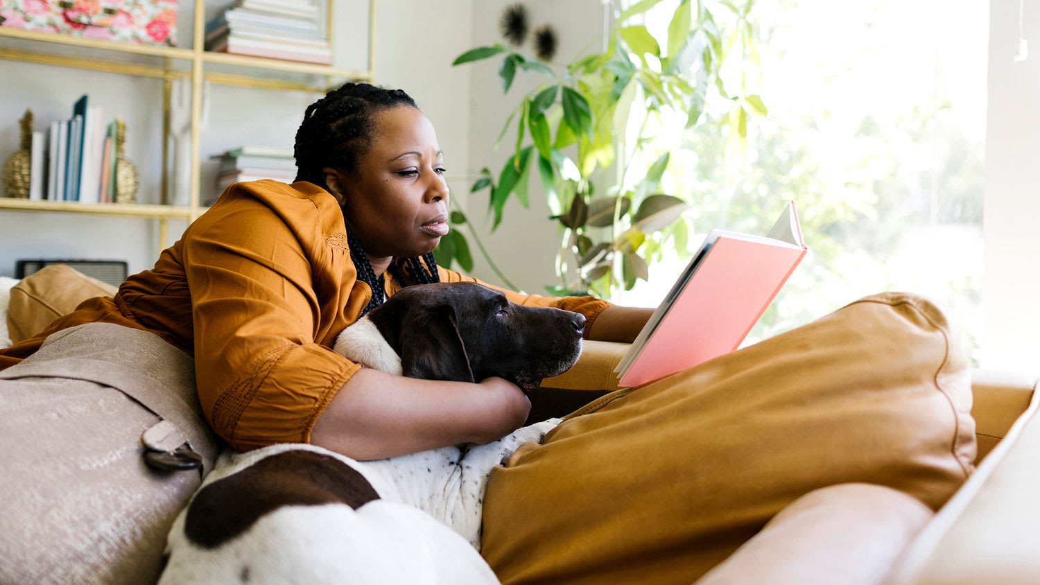 Woman reading book and snuggling with her dog