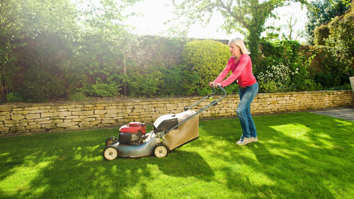 A mature woman mowing her garden’s lawn