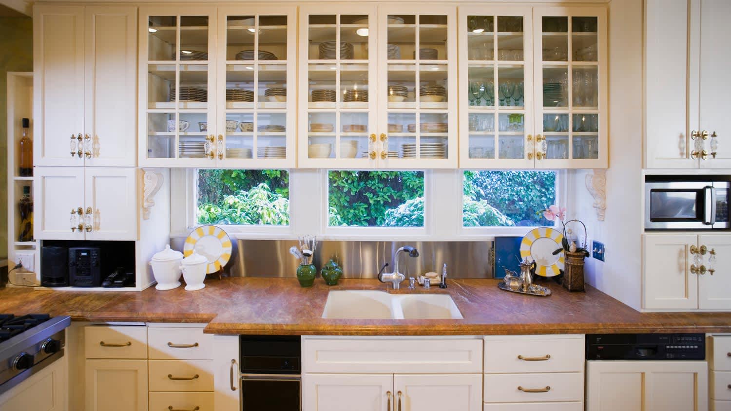 A kitchen with sink, countertop and glass door cabinets