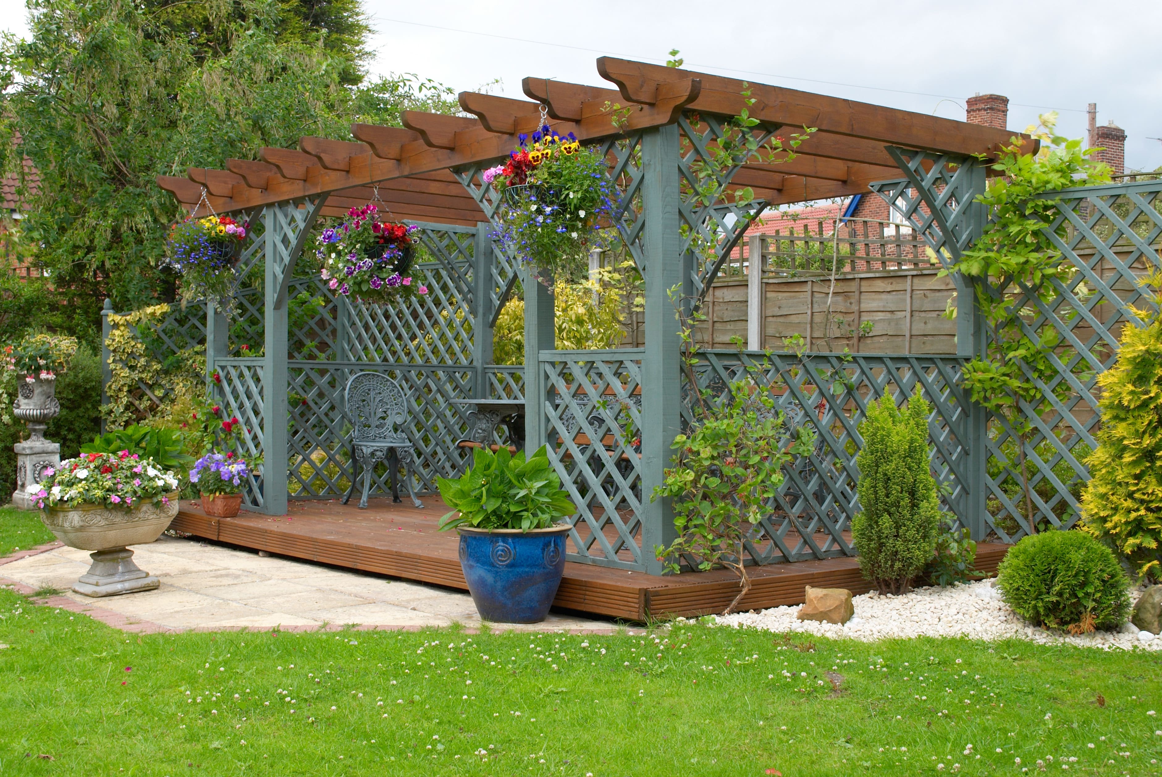Wooden pergola in backyard with green lattice walls and hanging plants