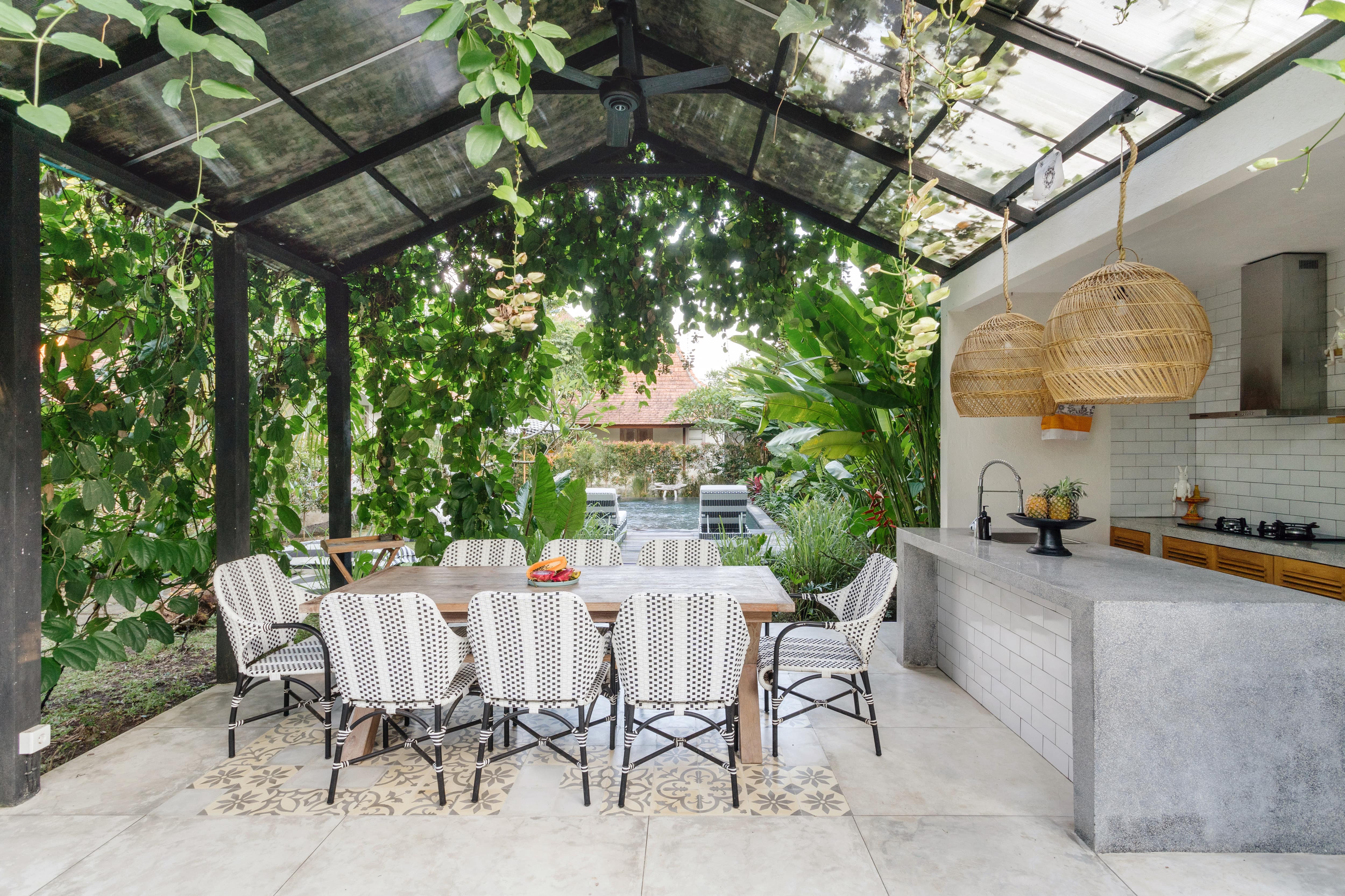 Black pergola with glass ceiling housing an outdoor kitchen and dining set