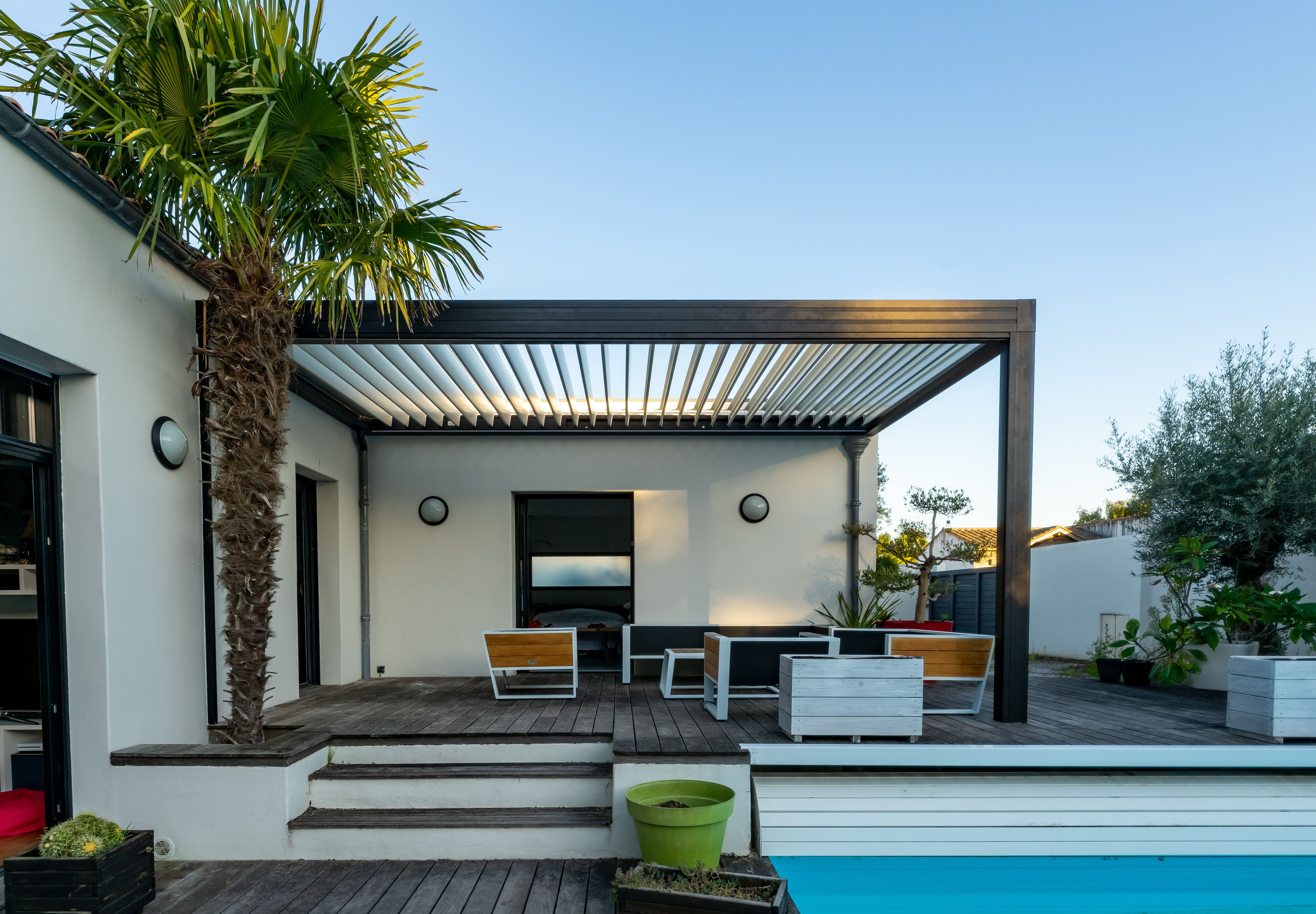 Dark, modern pergola with patio furniture under it next to a pool