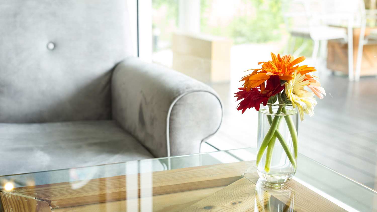 A vase with flowers on a wooden table with a glass tabletop