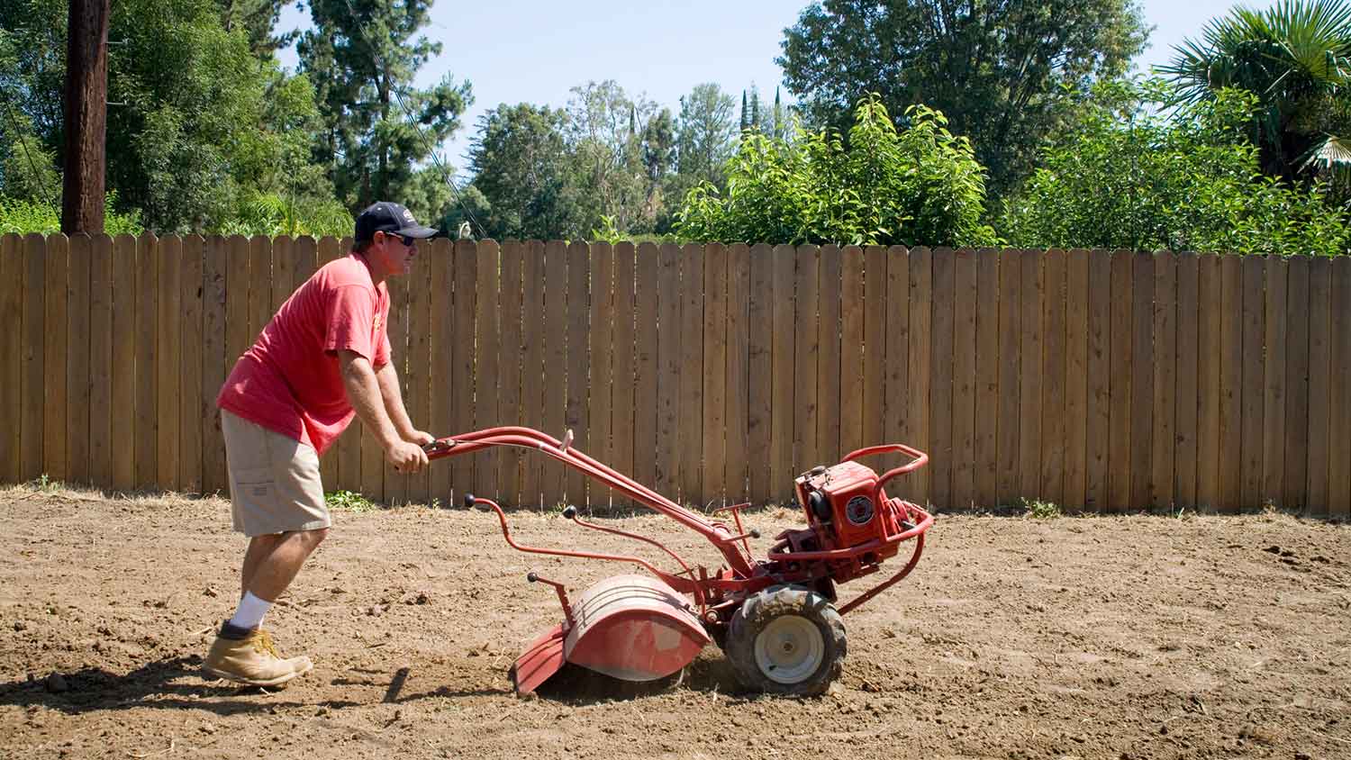 Man using rear-tine tiller in the backyard
