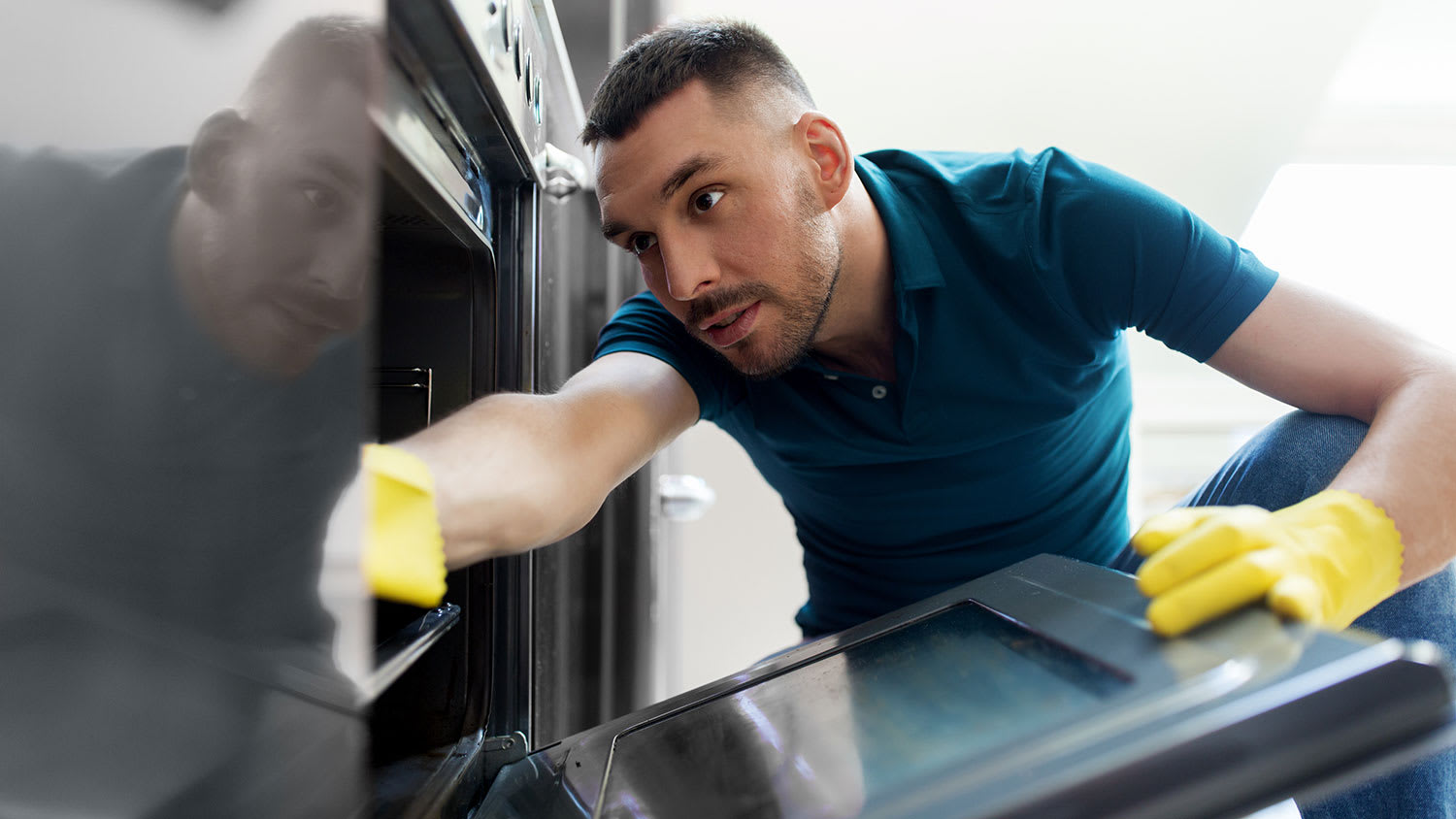 Man wearing rubber gloves scrubbing oven interior