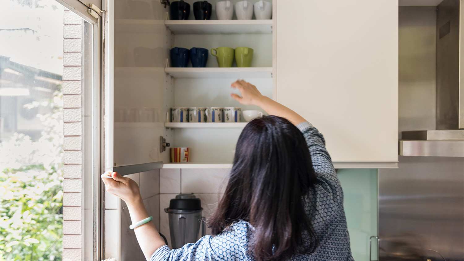 Woman open kitchen cabinet window mugs