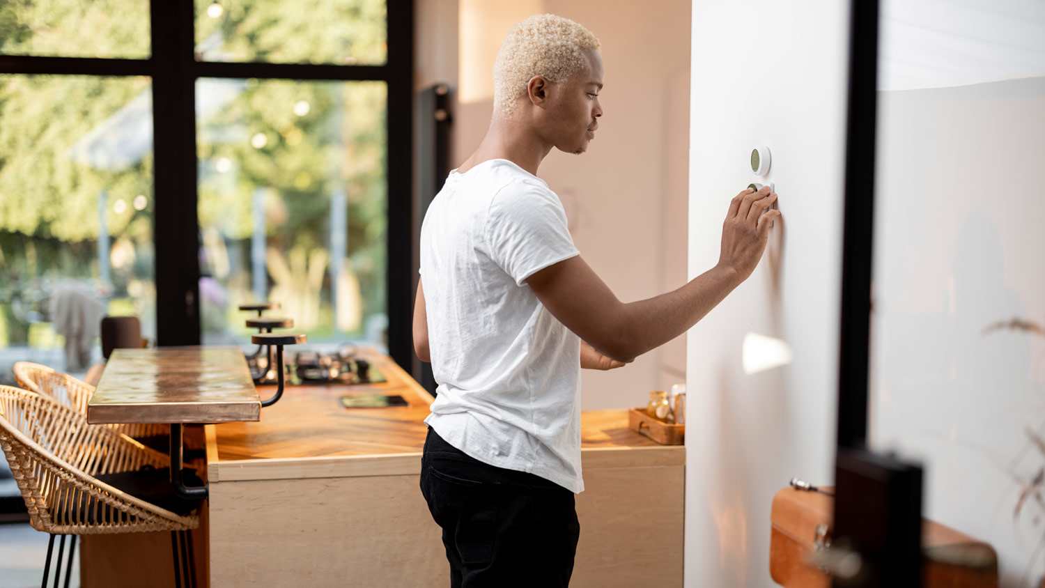 A young man adjusting the temperature on a thermostat