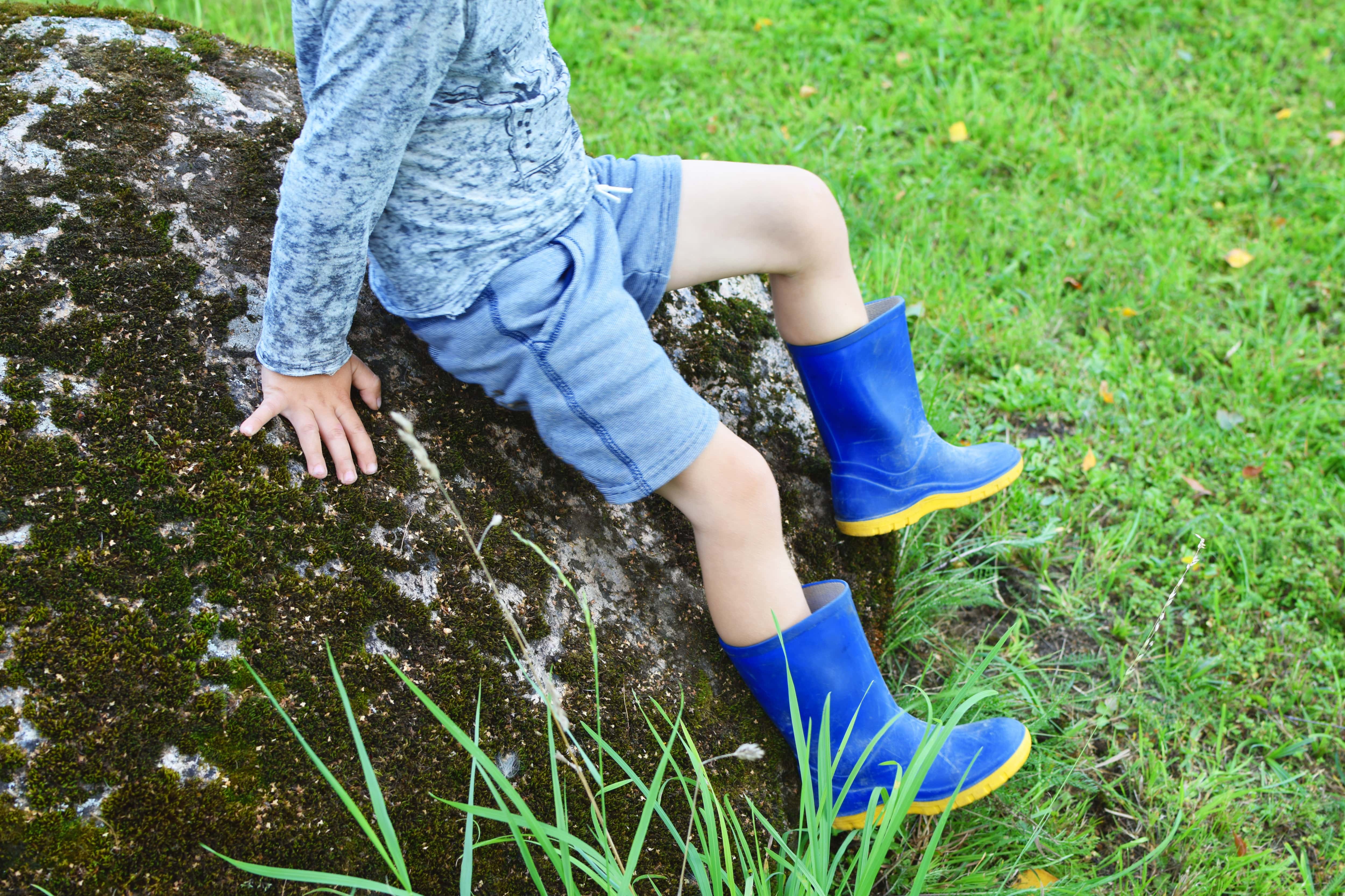 Boy sitting on a large rock in a yard