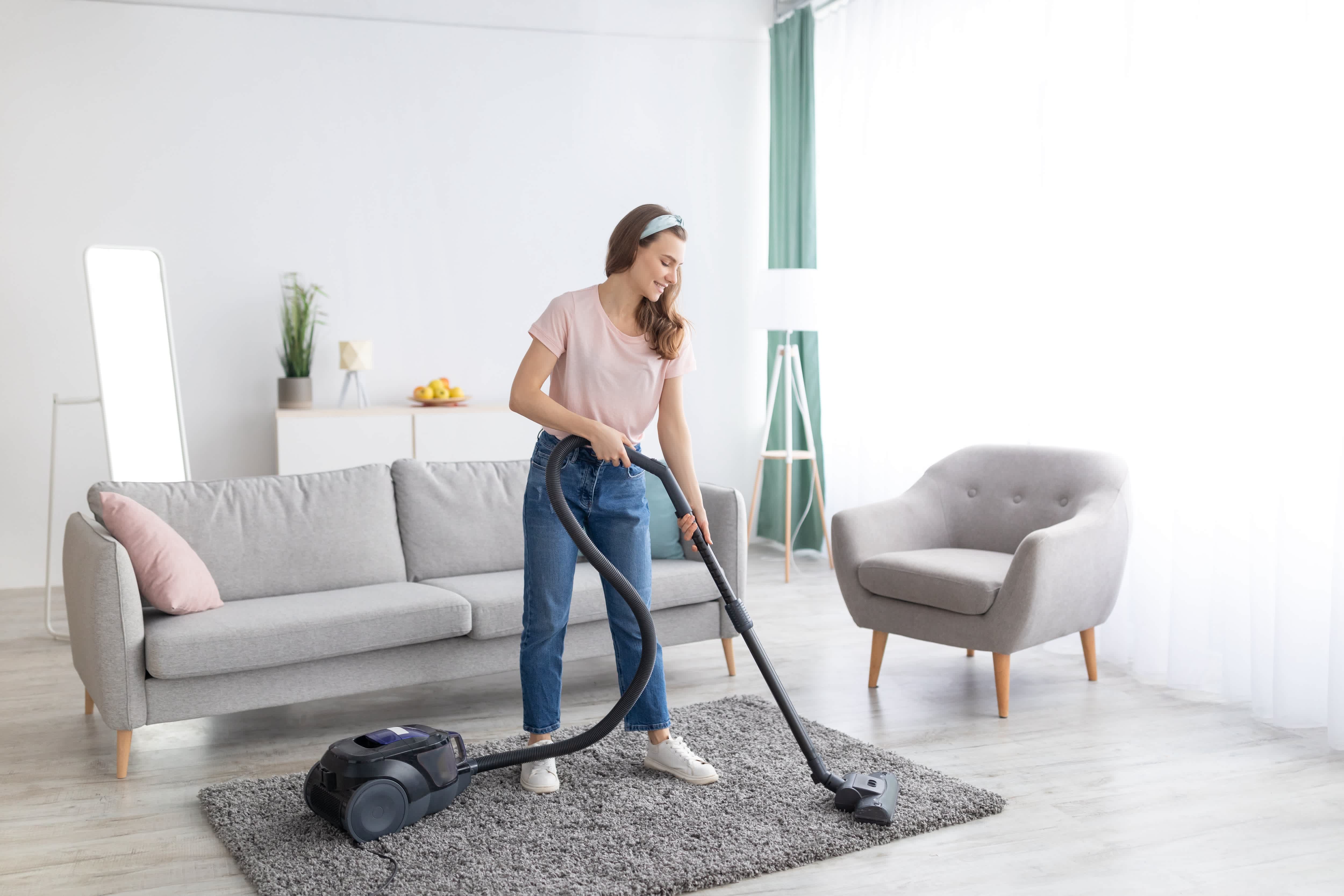 A young woman vacuuming a living room rug