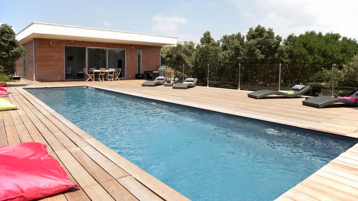 A lap pool and a wooden deck with lawn chairs