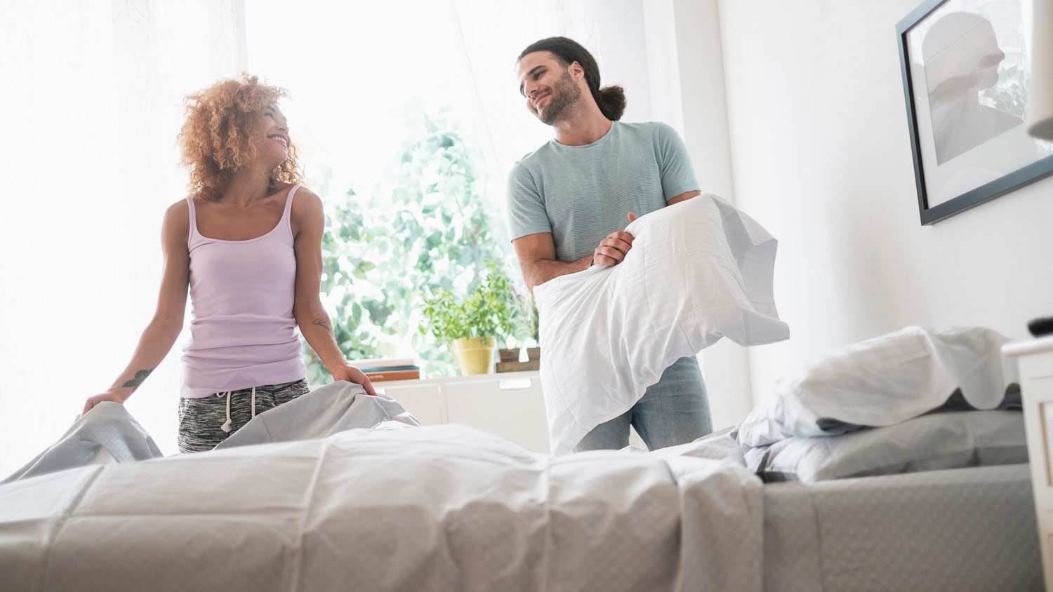 A young couple making the bed in the morning