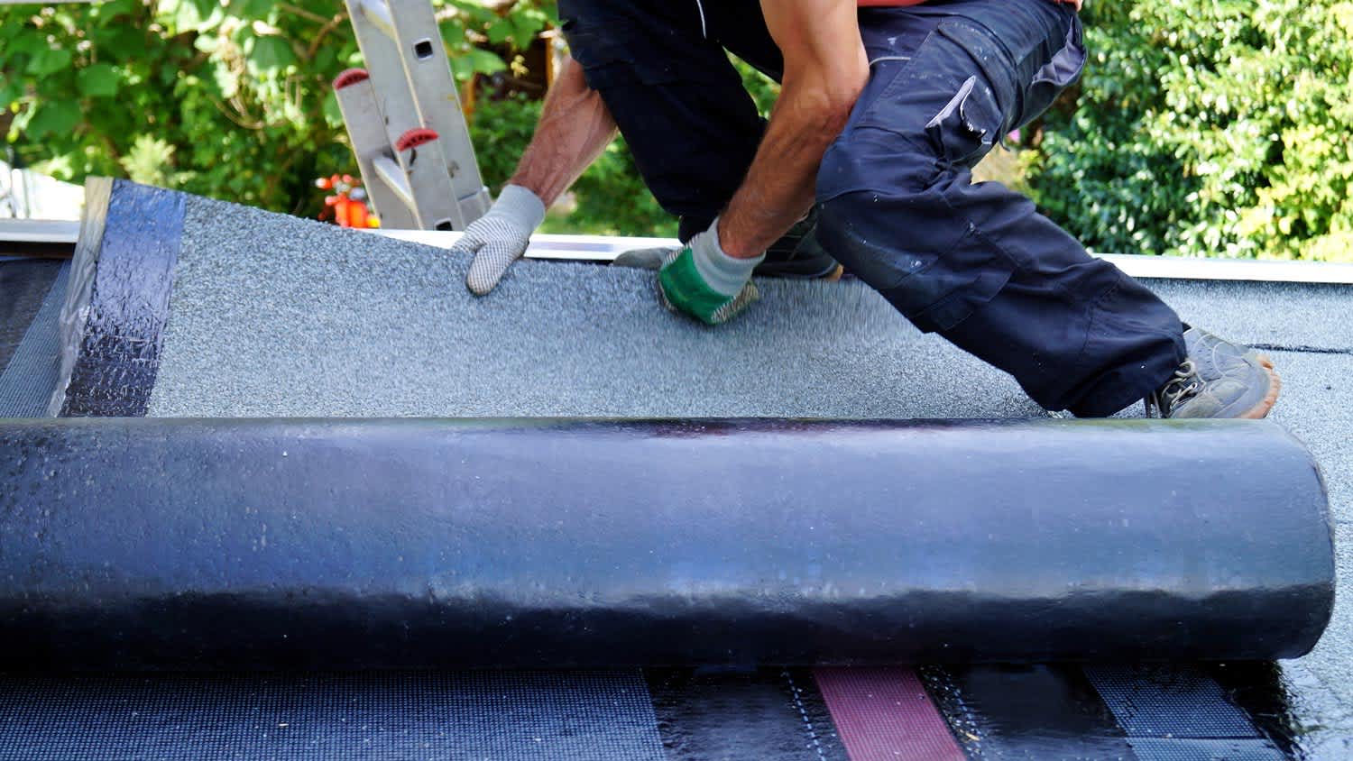 A worker laying a bitumen roll on the roof