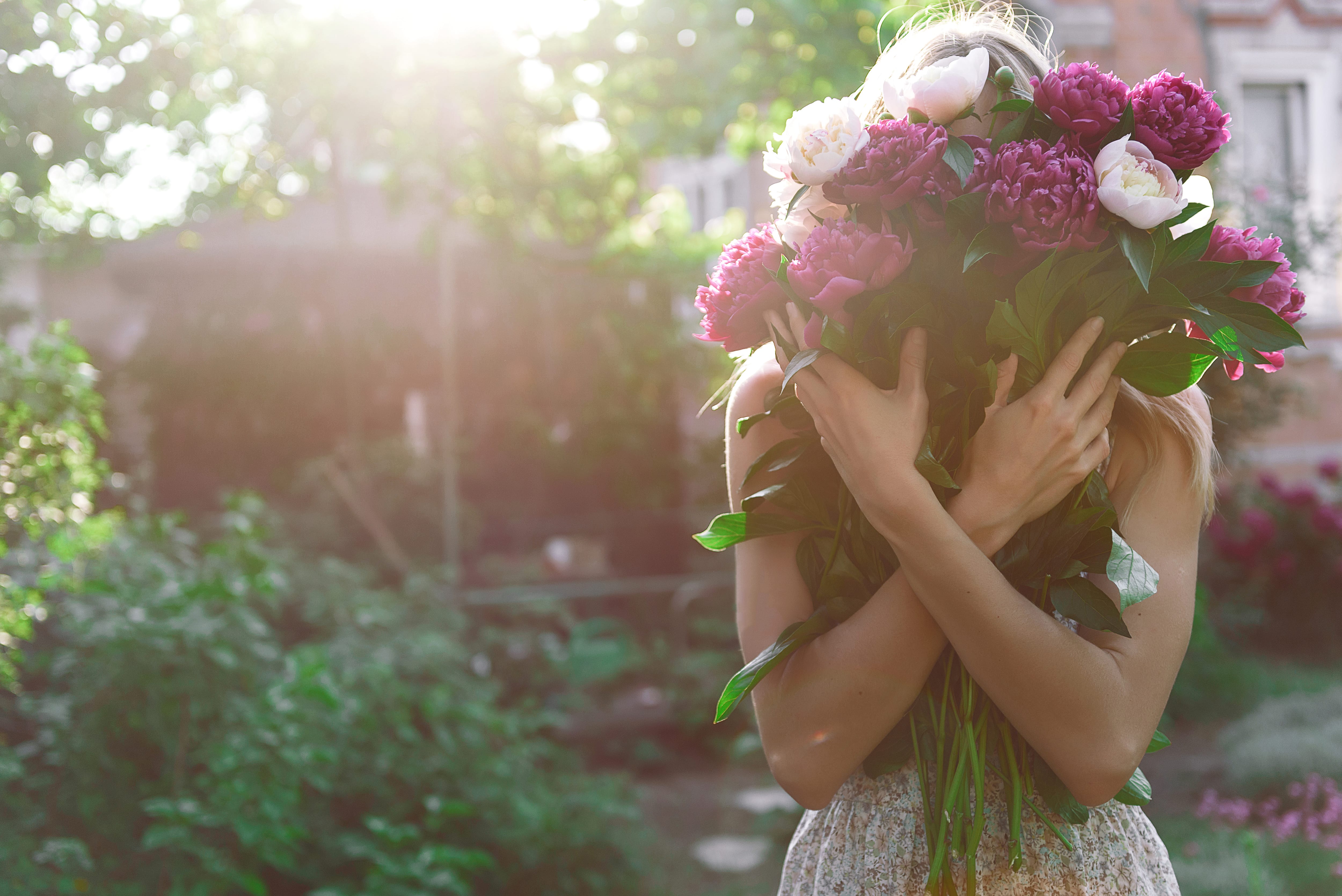 Woman holding a bouquet of peonies in a garden at sunset