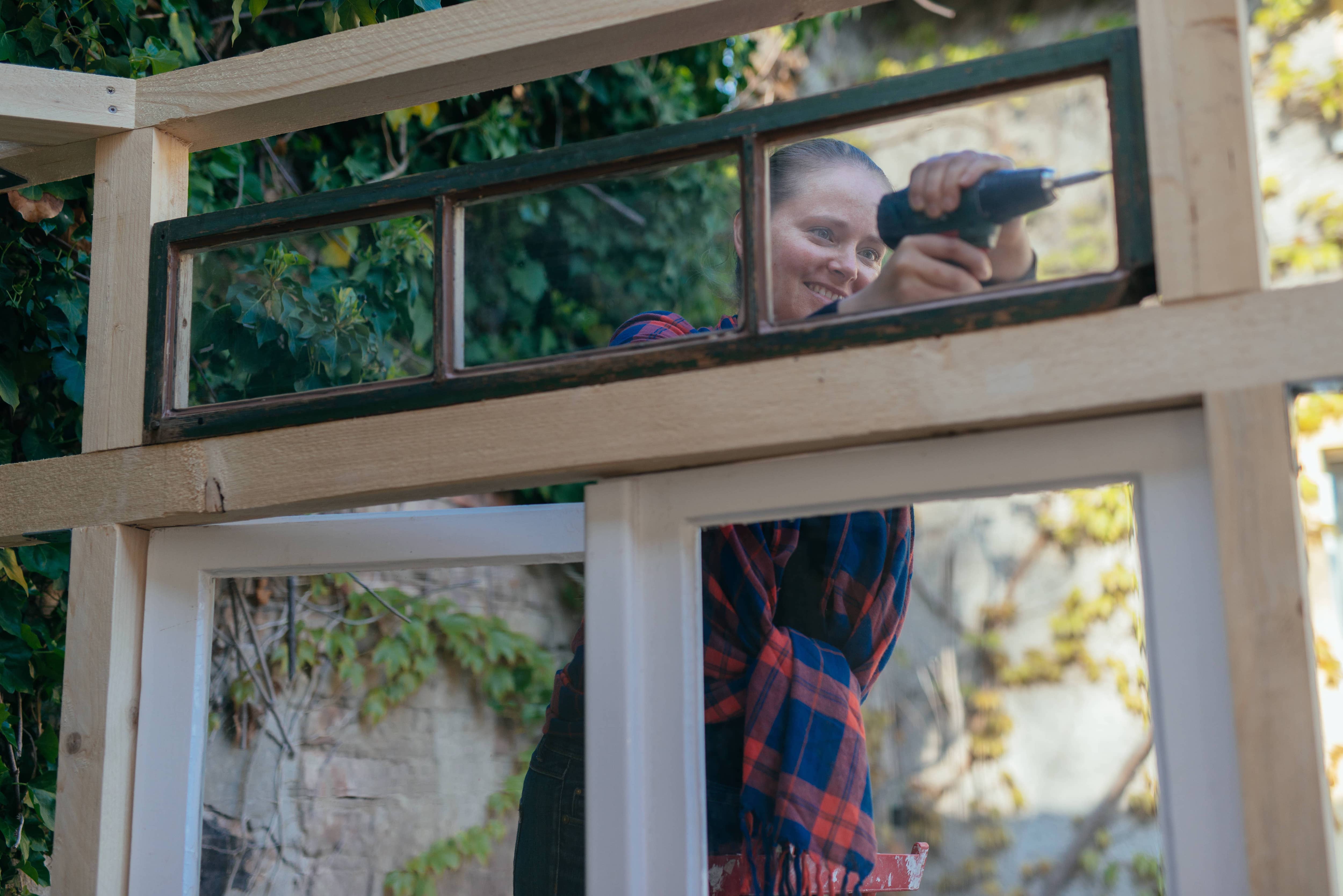 A woman installing a window the wood frame of a DIY greenhouse