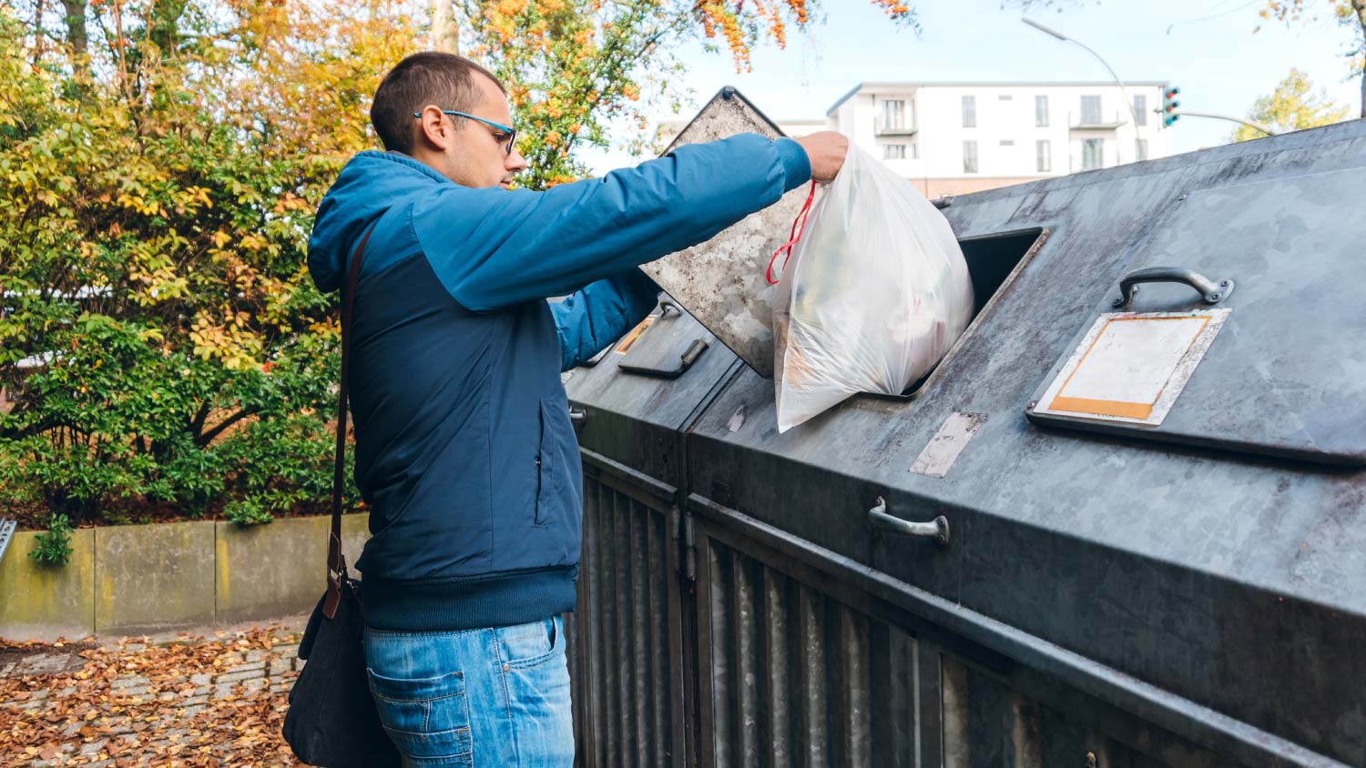 man throwing away garbage in dumpster
