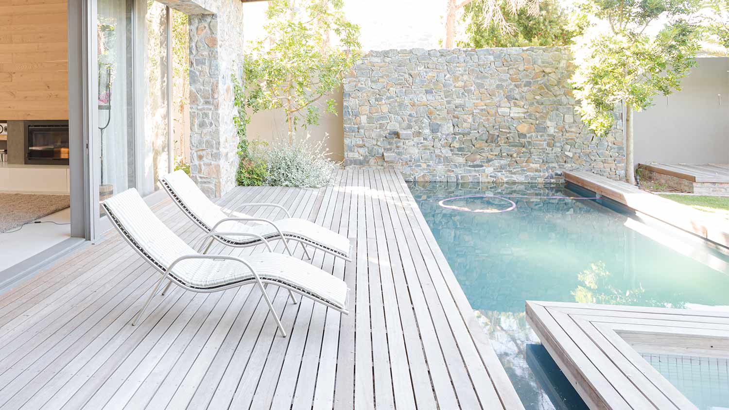 a light wood pool deck surrounding a square pool, with five deck chairs and grass