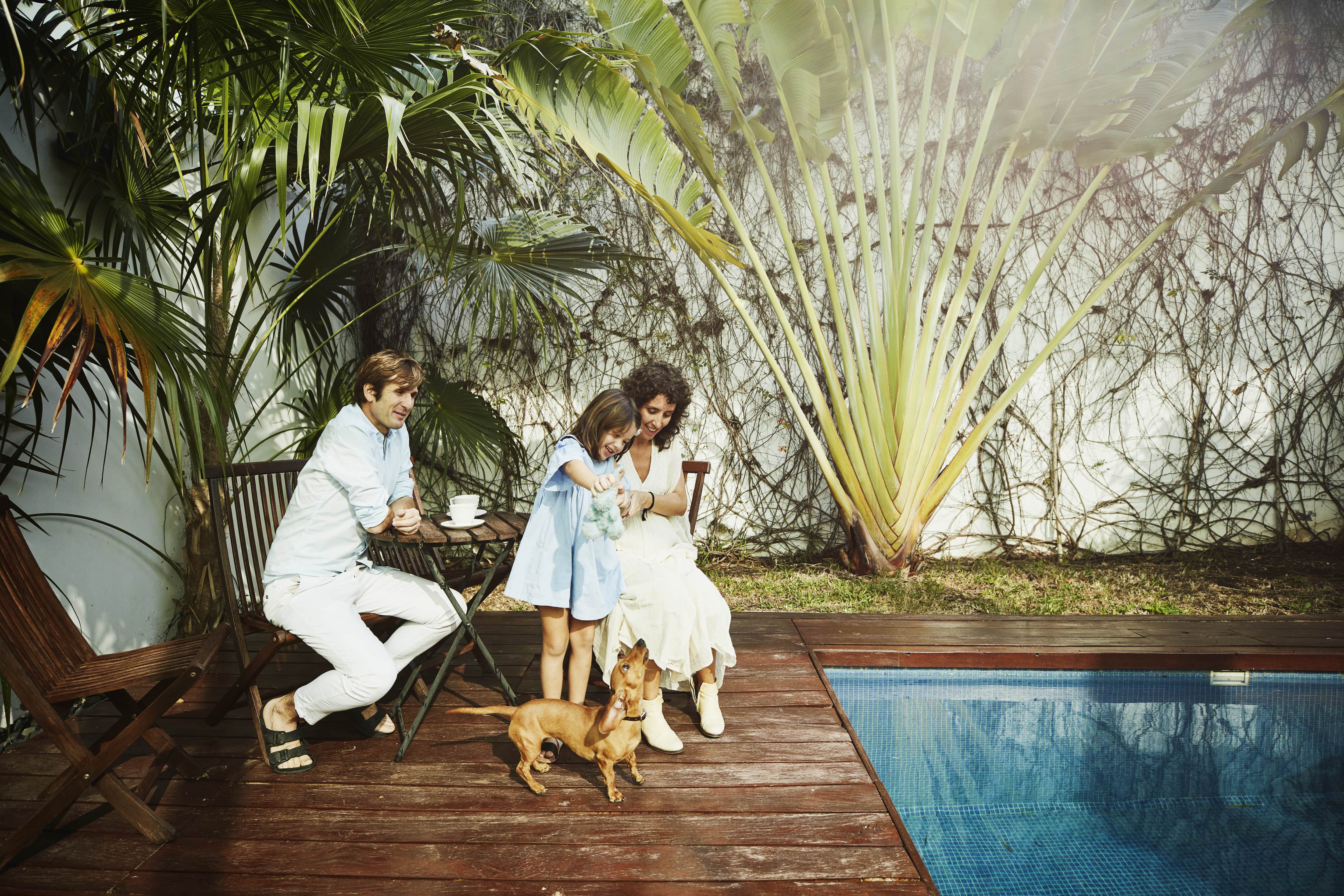 A young family and their dog sitting by their pool in the backyard