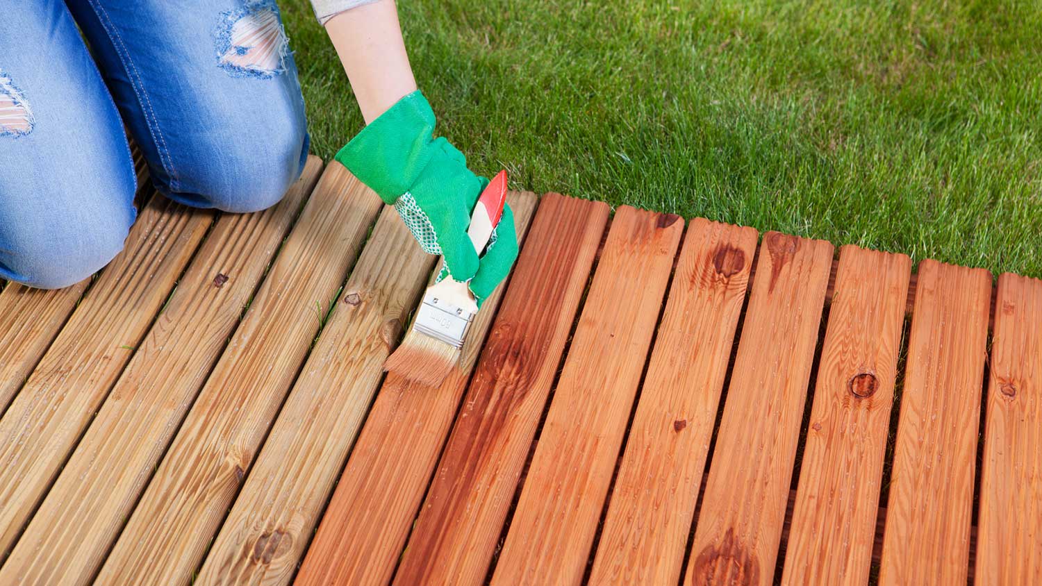 Woman applying varnish with a brush on wooden deck