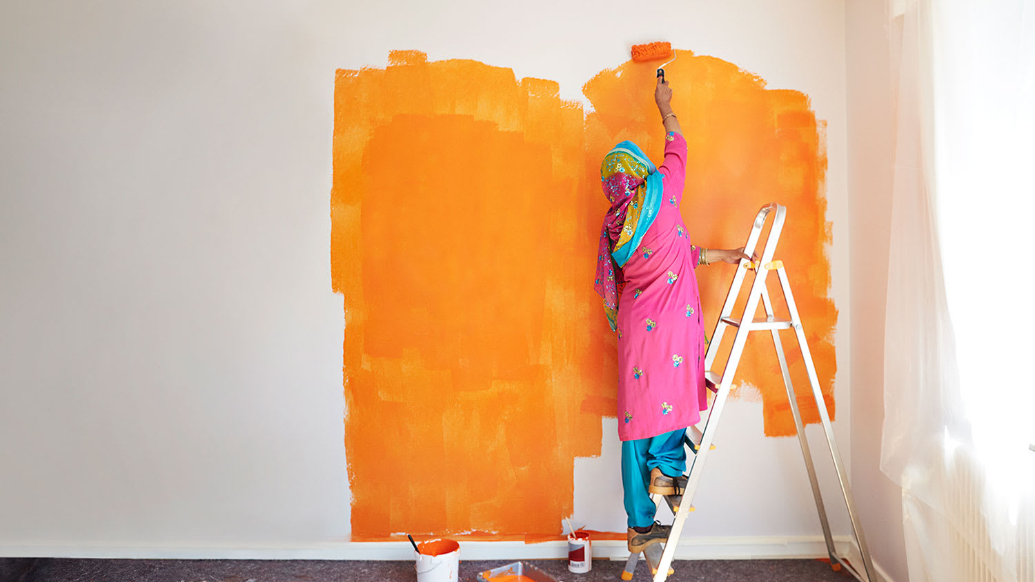 a woman in overalls painting a white wall with green paint and smiling