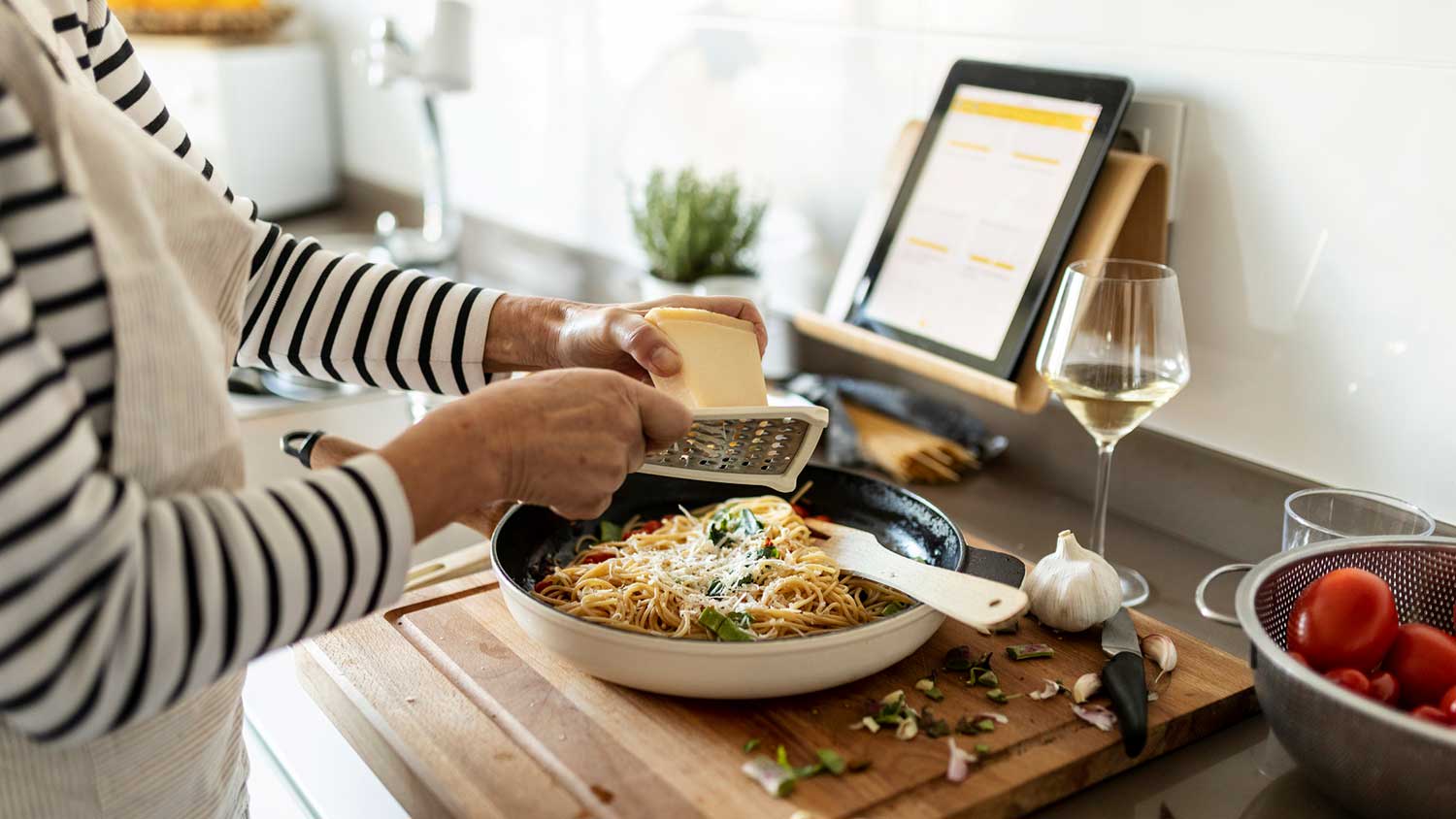 Woman shredding cheese on top of a pasta dish