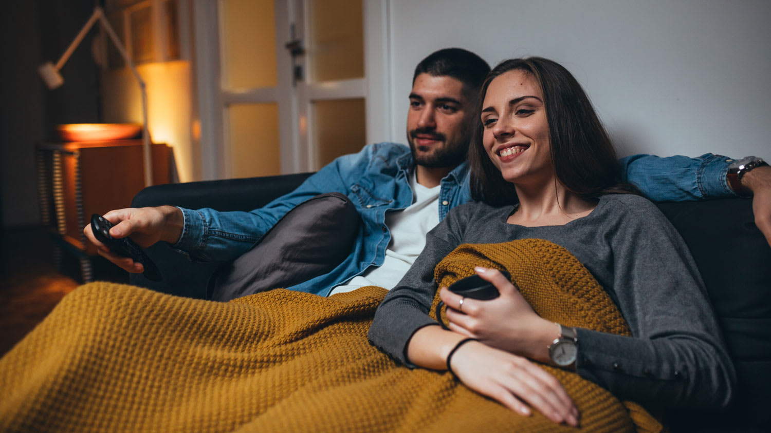 A young couple covered in a blanket watching tv