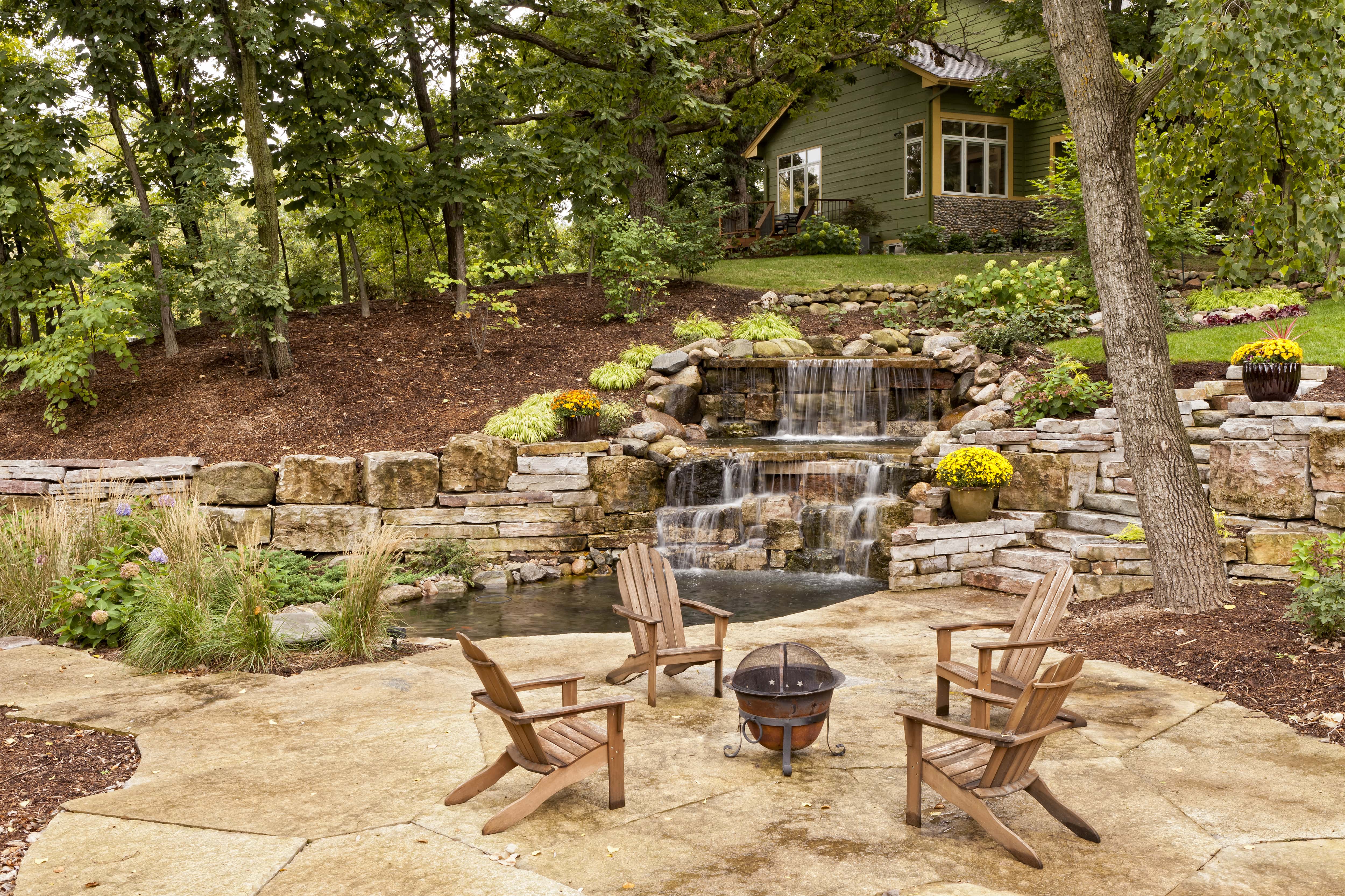 A luxury backyard waterfall with landscaping and a stone patio