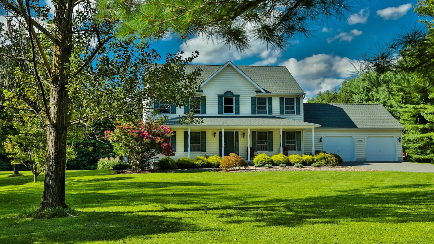 The exterior of a house on a sunny day with beautiful lawn and a big tree