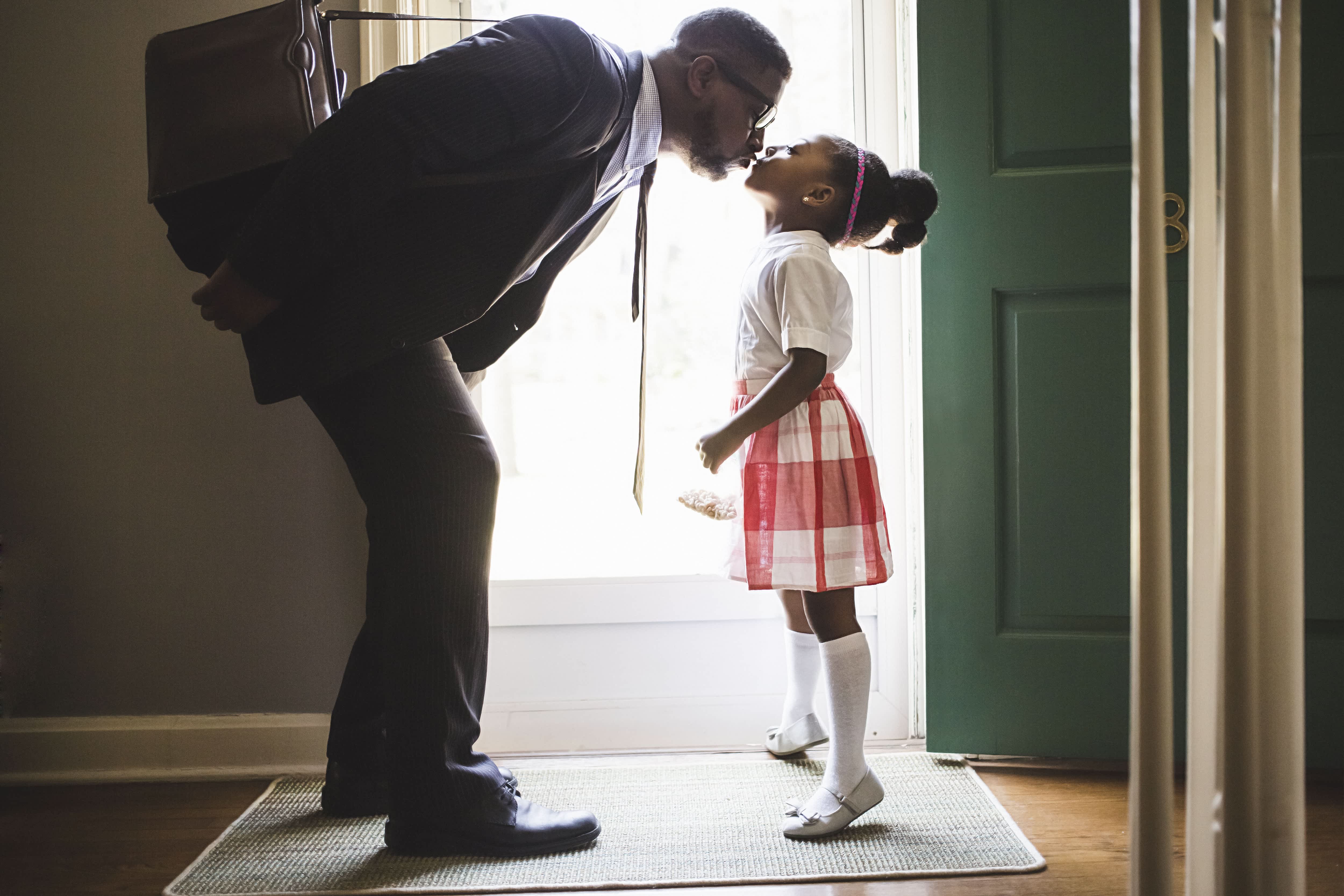 Father and daughter kissing goodbye in front of door