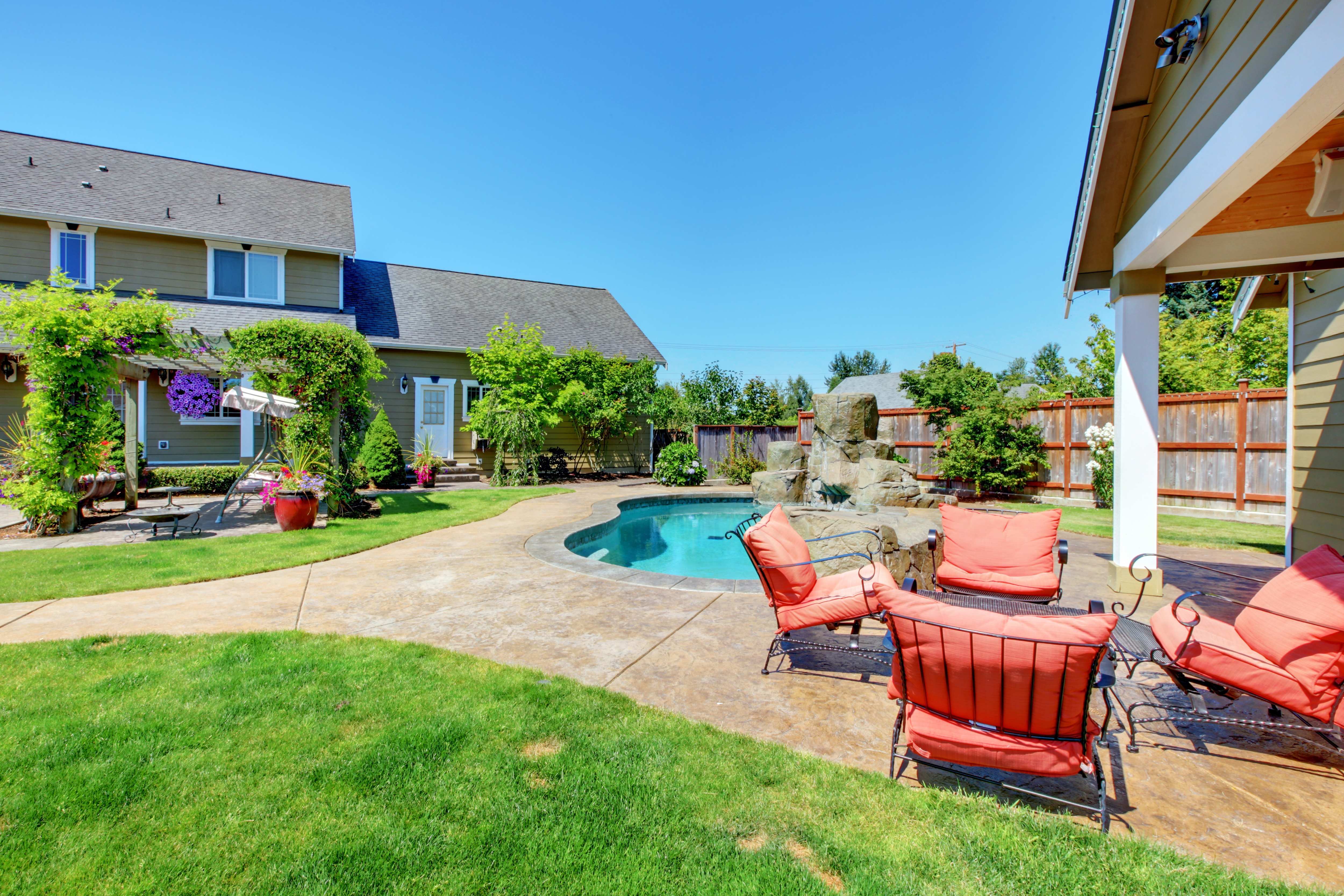 A residential backyard with an inground pool and a pool house with an extended roof