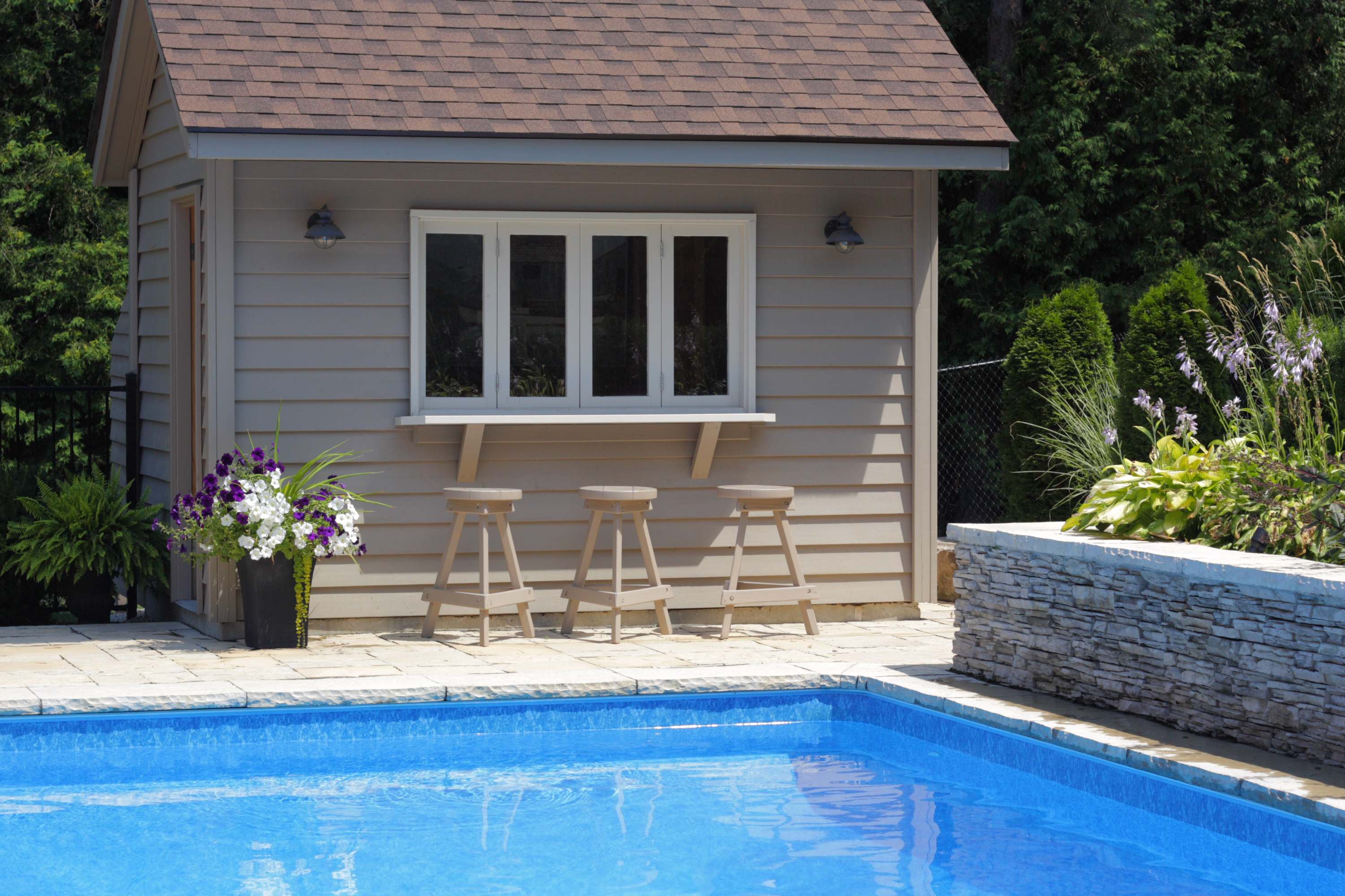A pool house with an attached bar, bar stools, and a sliding window
