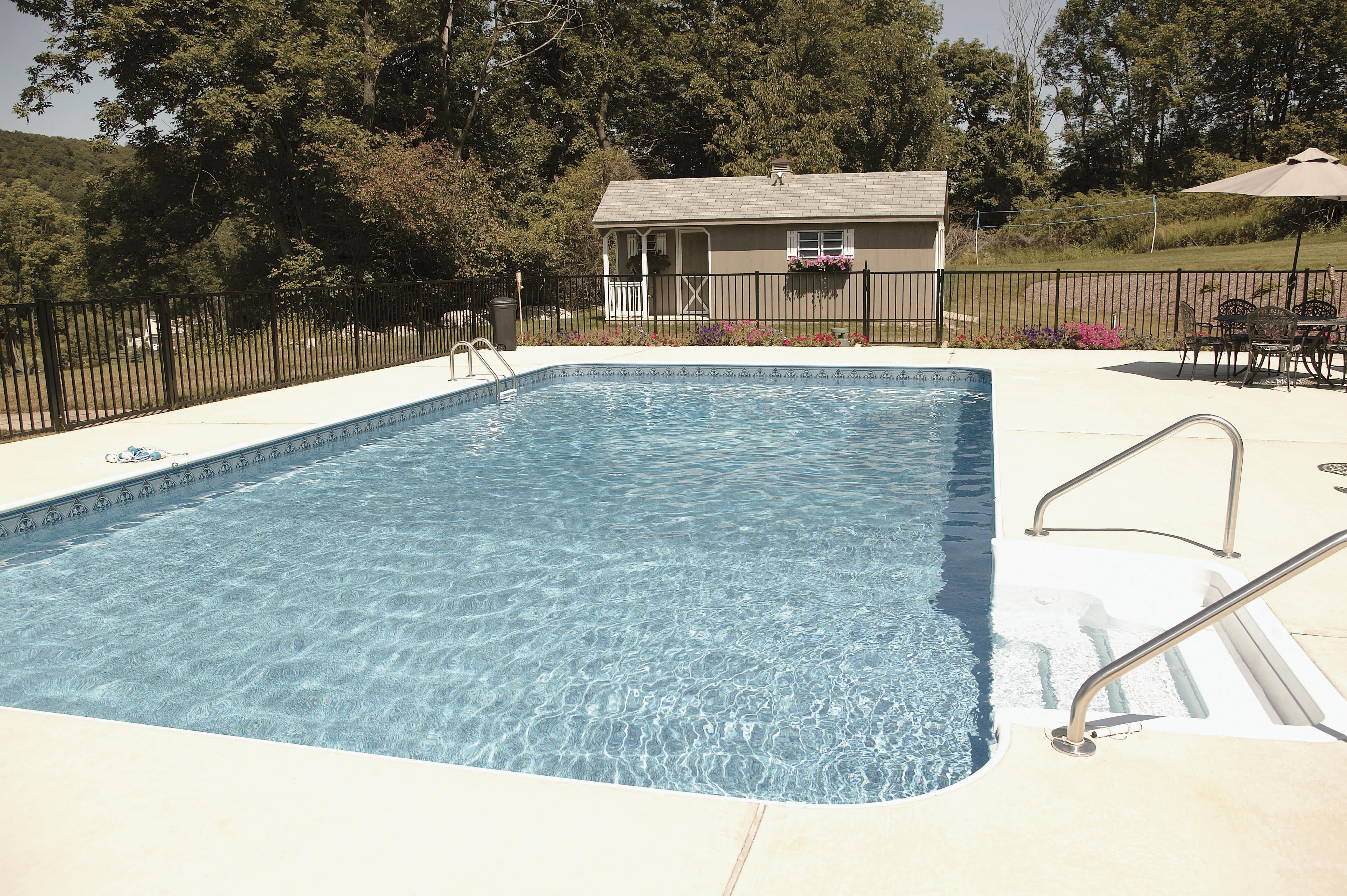 A large country side inground pool with a small porch