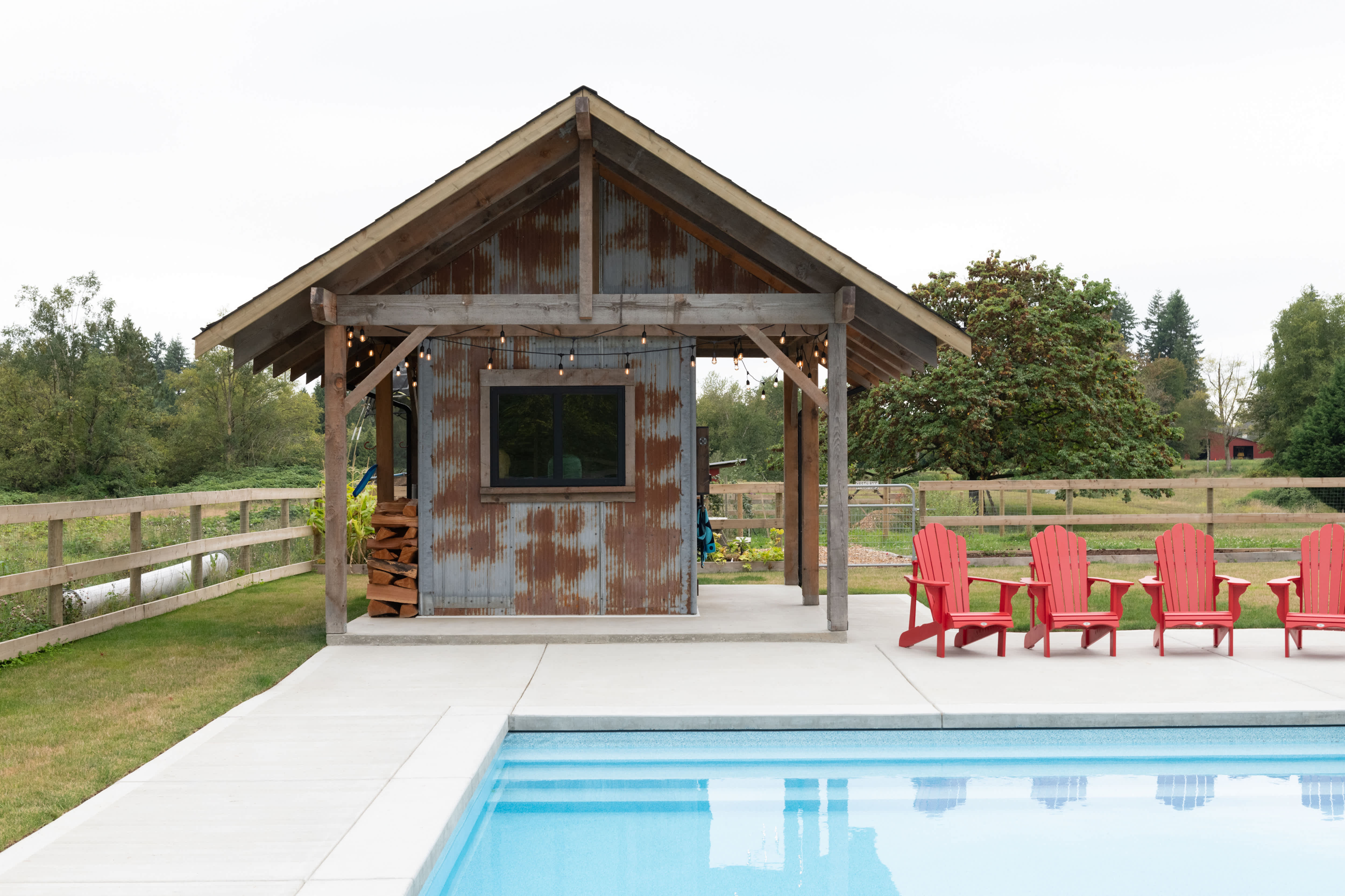 An inground pool with a rustic pool house built with repurposed materials