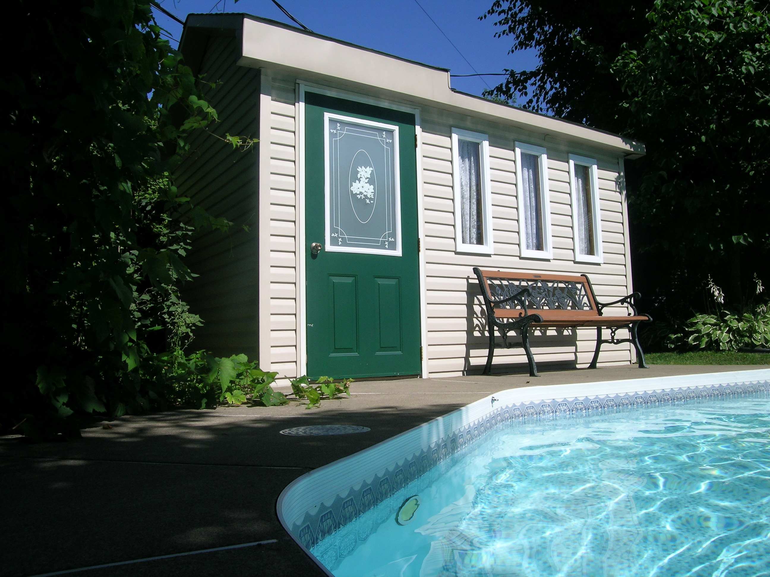 A tiny house with siding and a green door near an inground pool