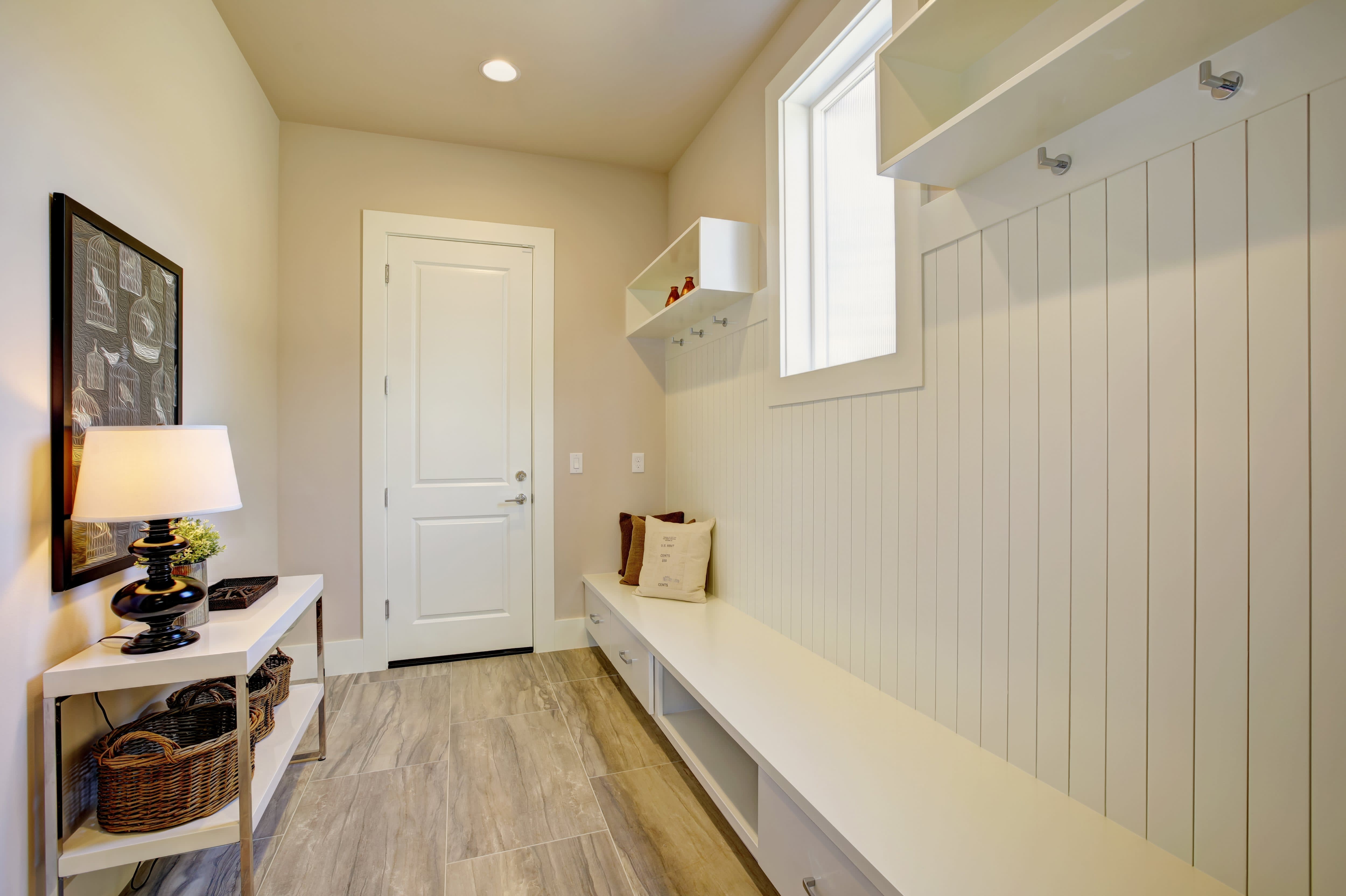 Crisp white mudroom with beadboard wainscoting on top of additional baseboard shelving