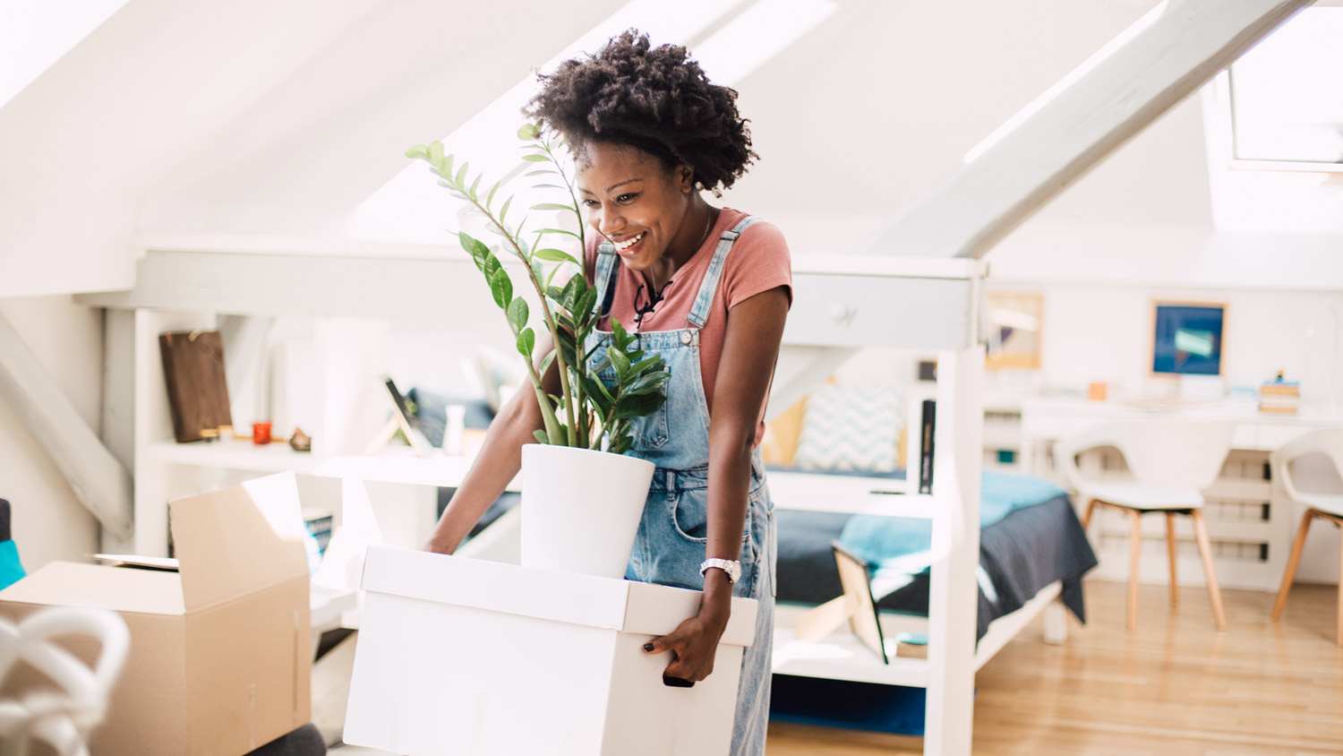 A happy woman holding a box and a plant moving in her new apartment