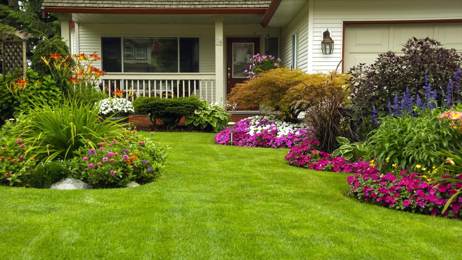 A landscaped garden with flowers in front of a white porch